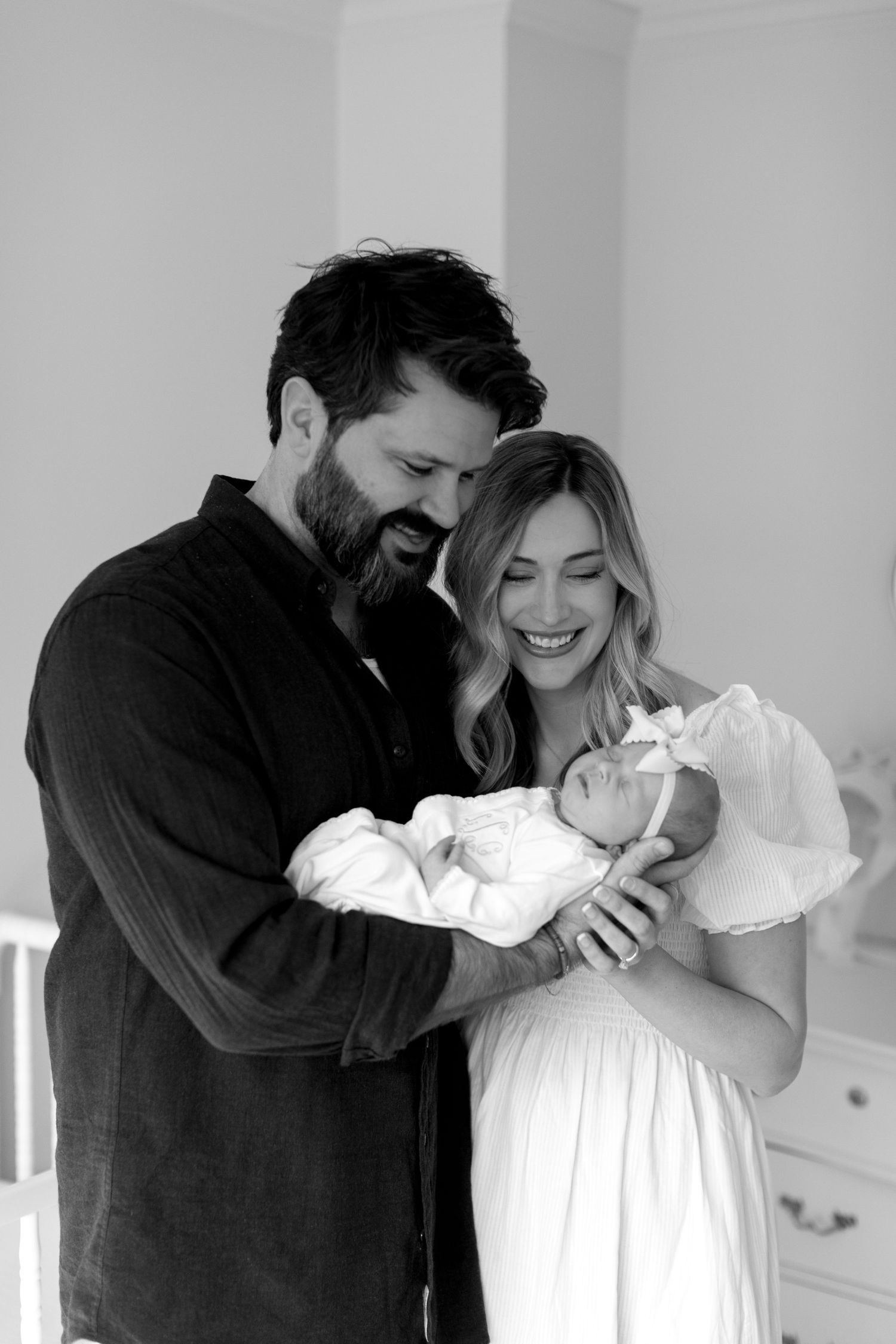 Black and white photos capturing intimate family moments with a newborn in a white dress.