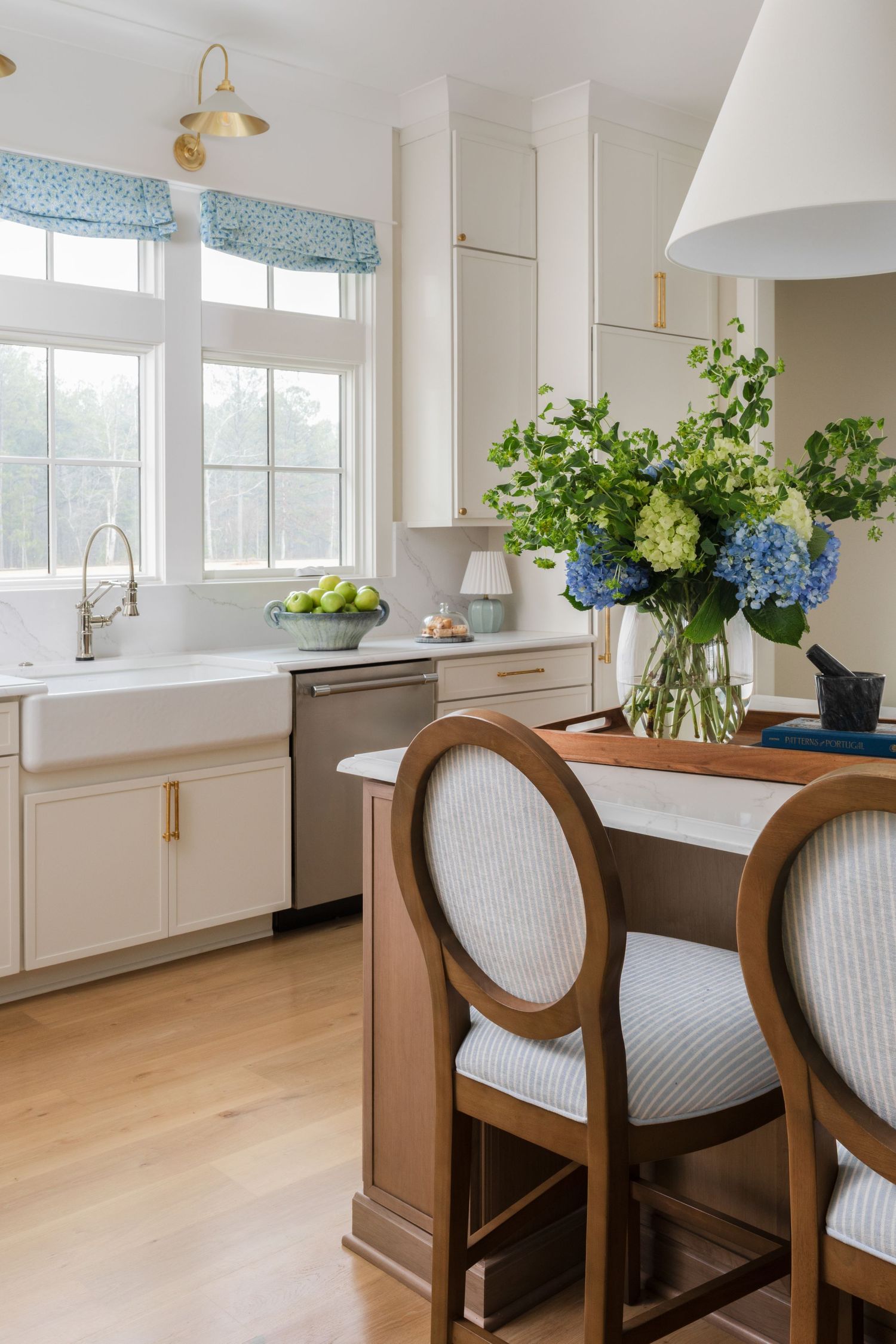 Modern coastal kitchen features white cabinets, wood island with upholstered barstools, and blue hydrangea centerpiece.