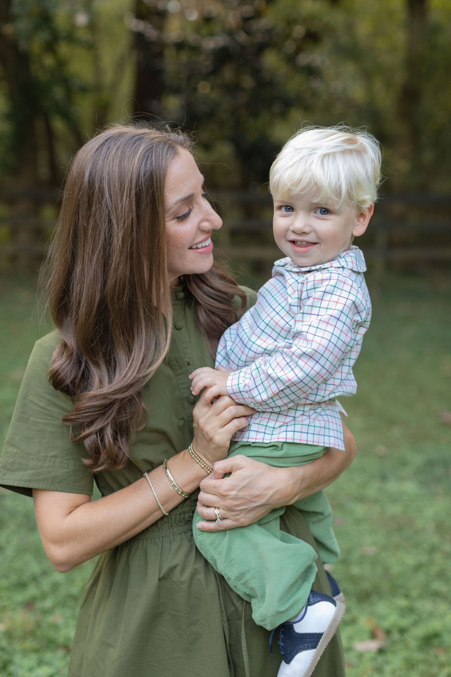 A woman in an olive green shirt shares playful moments with a young child wearing a checkered shirt outdoors.