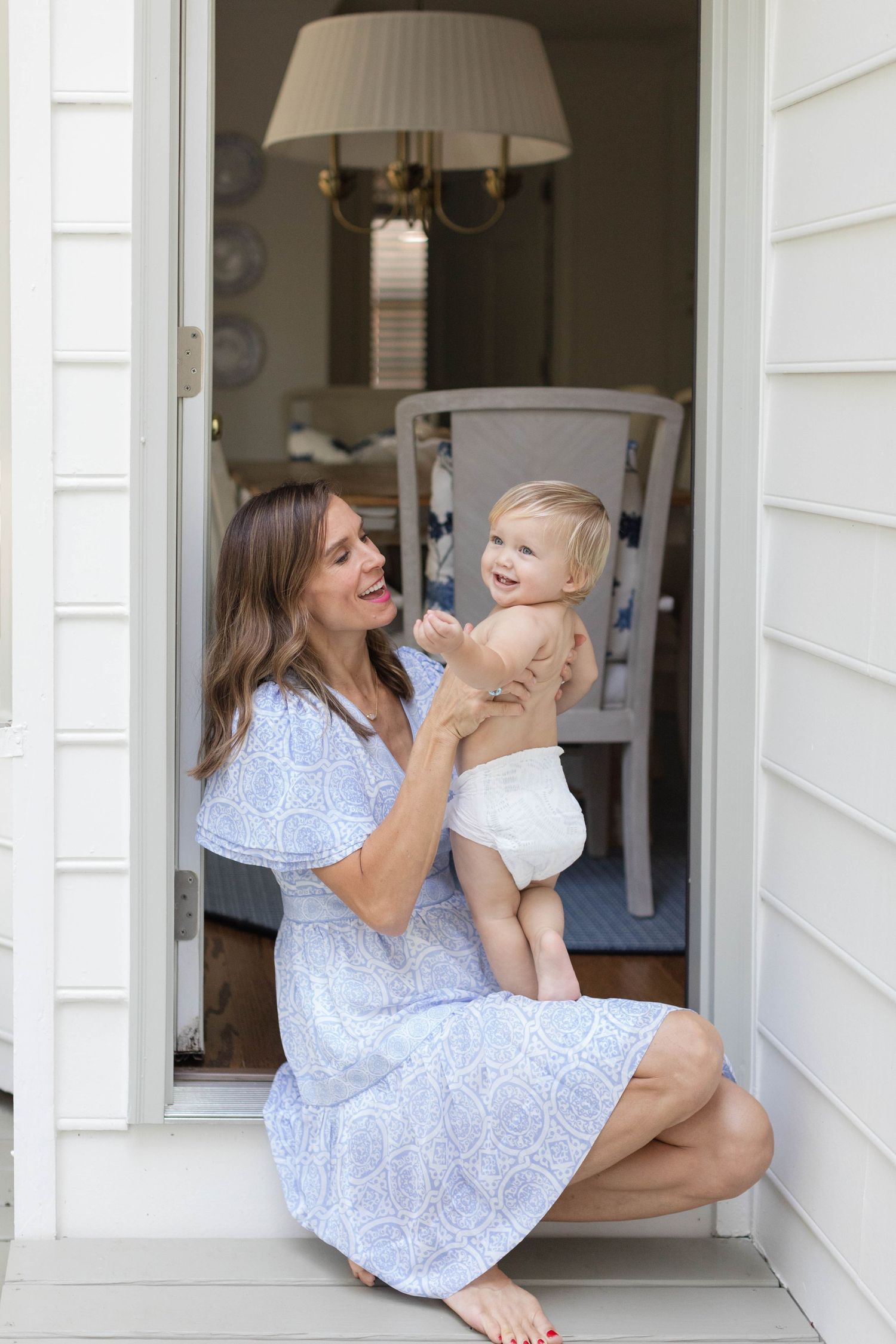 A parent in a light blue dress sits with their baby on a doorstep in a sweet candid moment series.