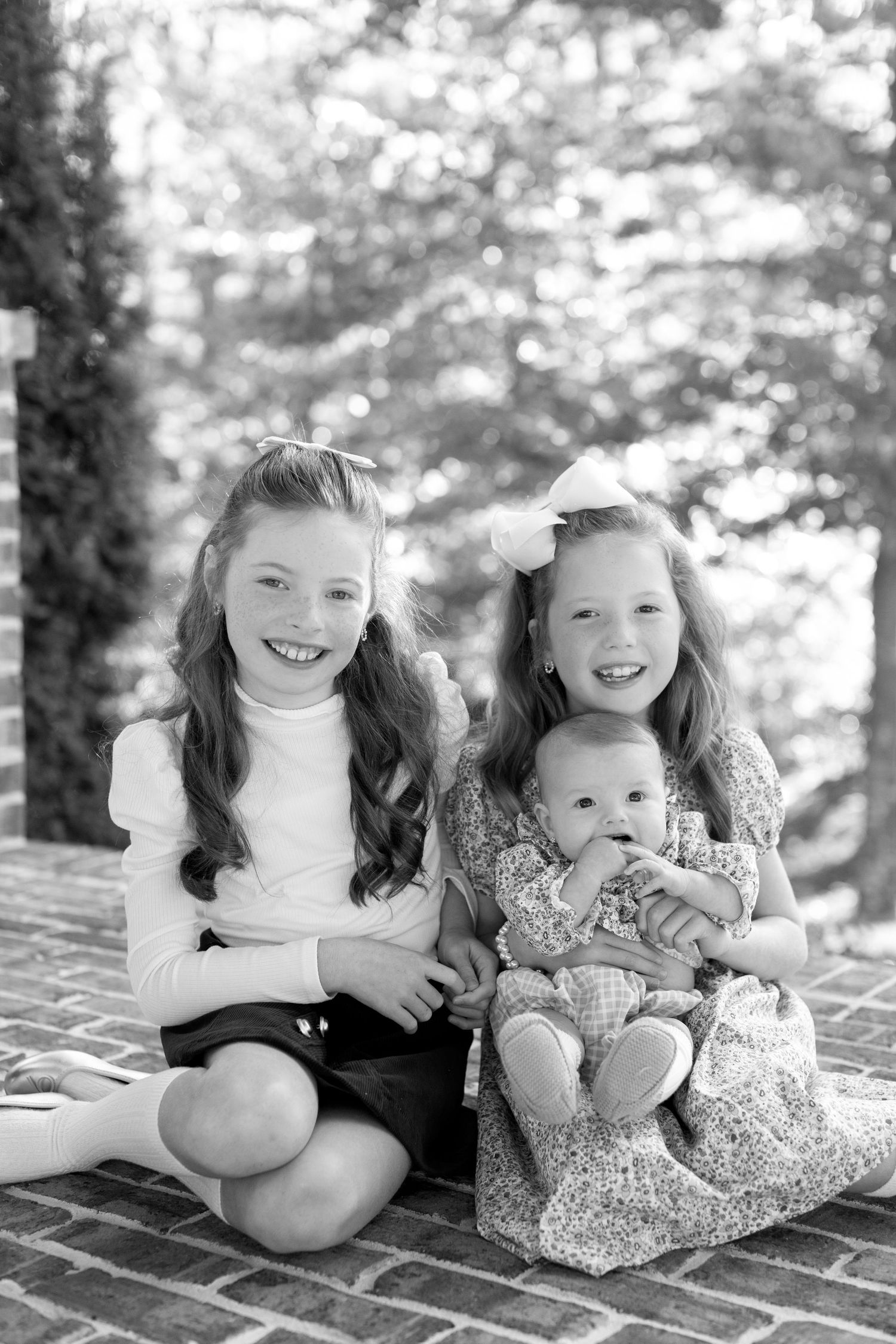 Black and white photo series showing two young children sitting together on brick steps, smiling and playing.