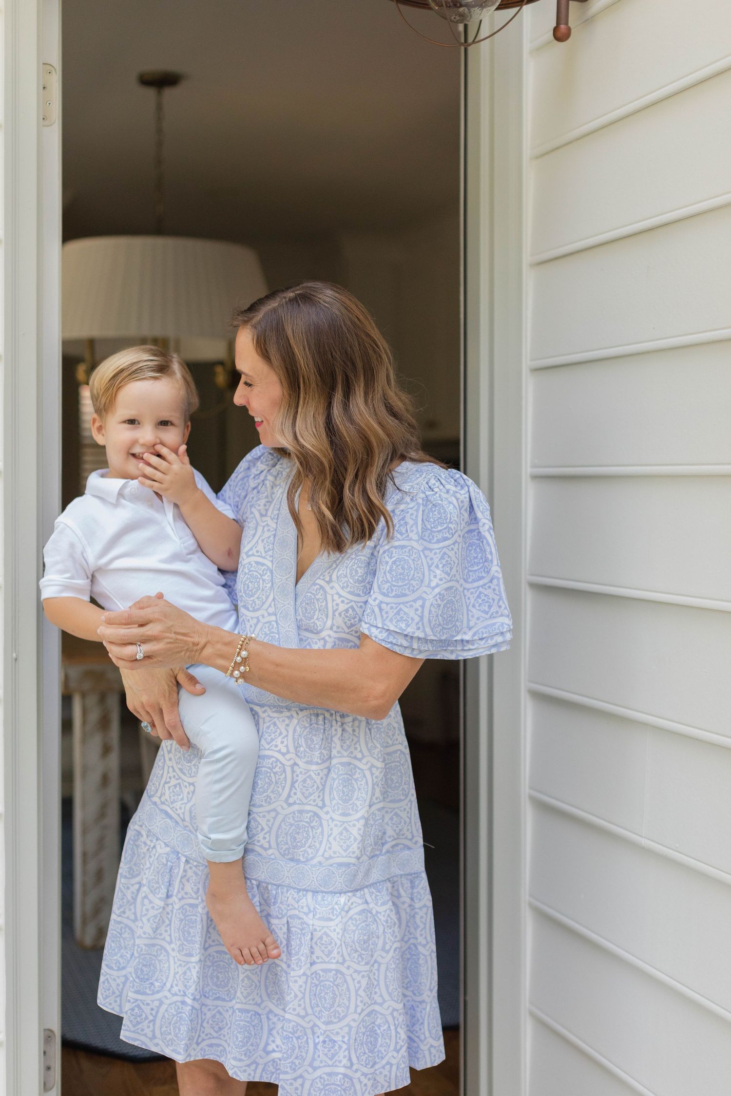 Mother and child in matching blue dresses share joyful moments on front porch.