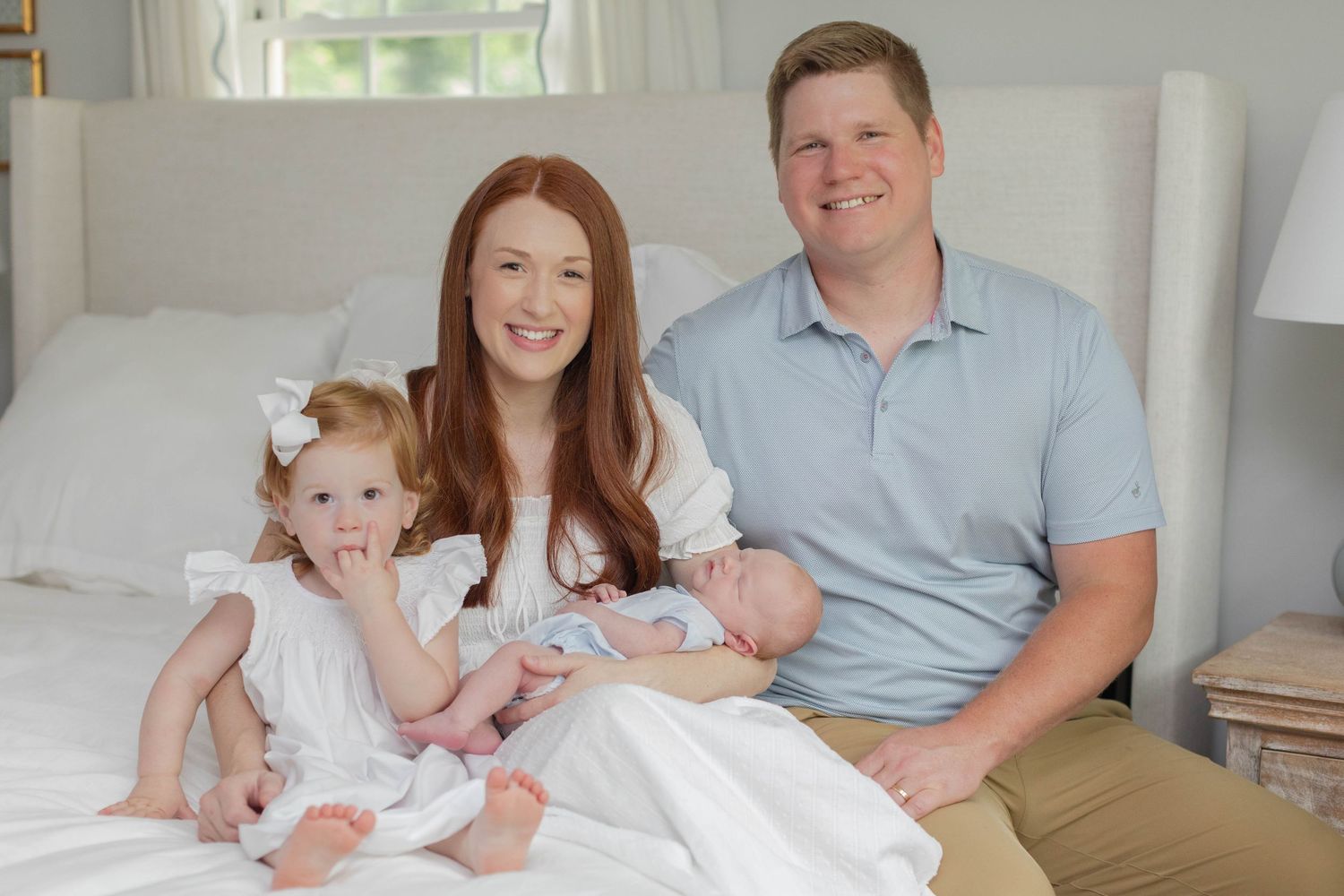 A sweet newborn photoshoot in a bright bedroom features tender family moments on white bedding.