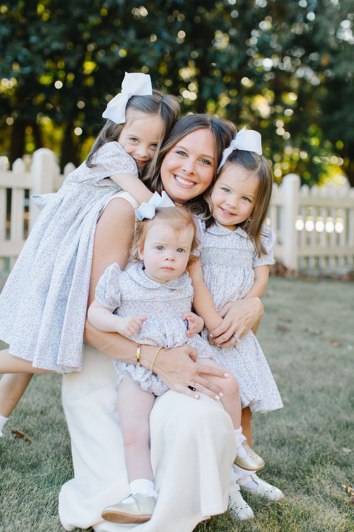 A sweet family moment captured outdoors with matching white dresses against a picturesque white fence and natural backdrop.