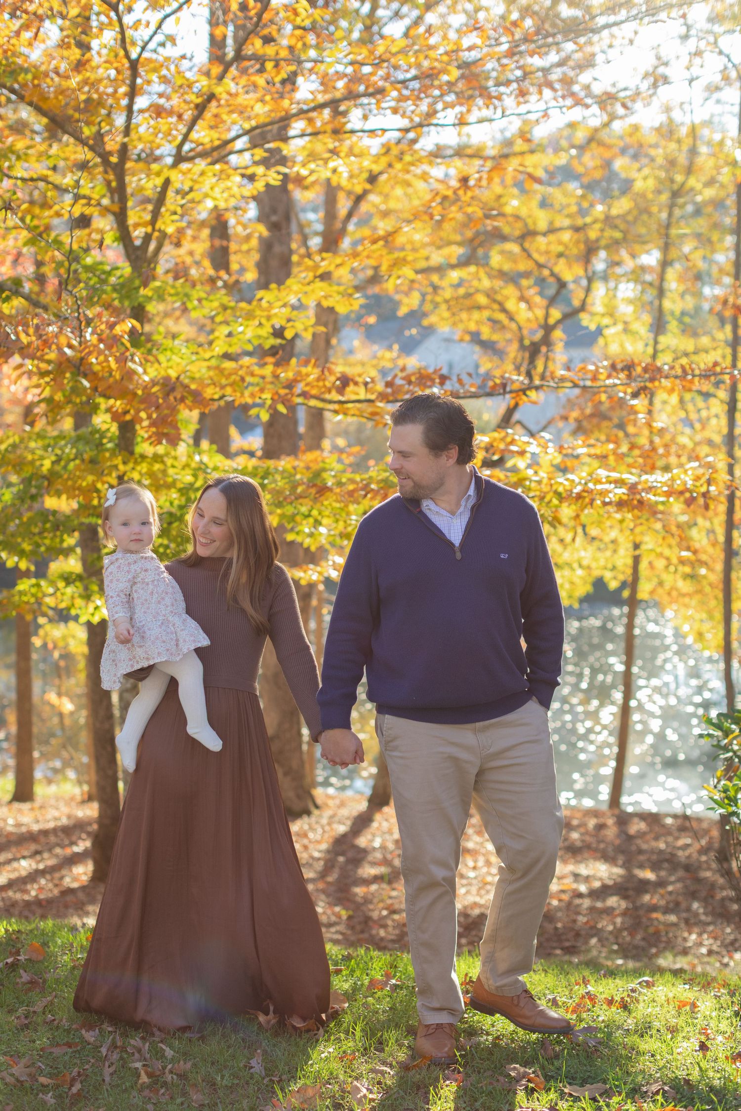 A family walks together through a sunlit autumn forest with golden leaves and warm afternoon light filtering through trees.