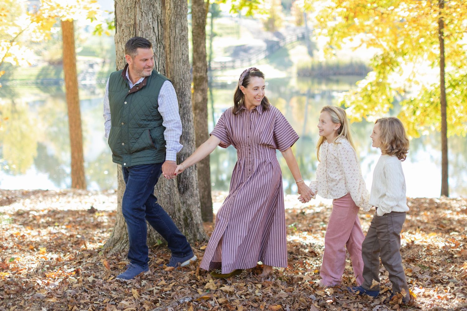 Family wearing coordinated fall outfits plays together in autumn leaves during outdoor photo session.