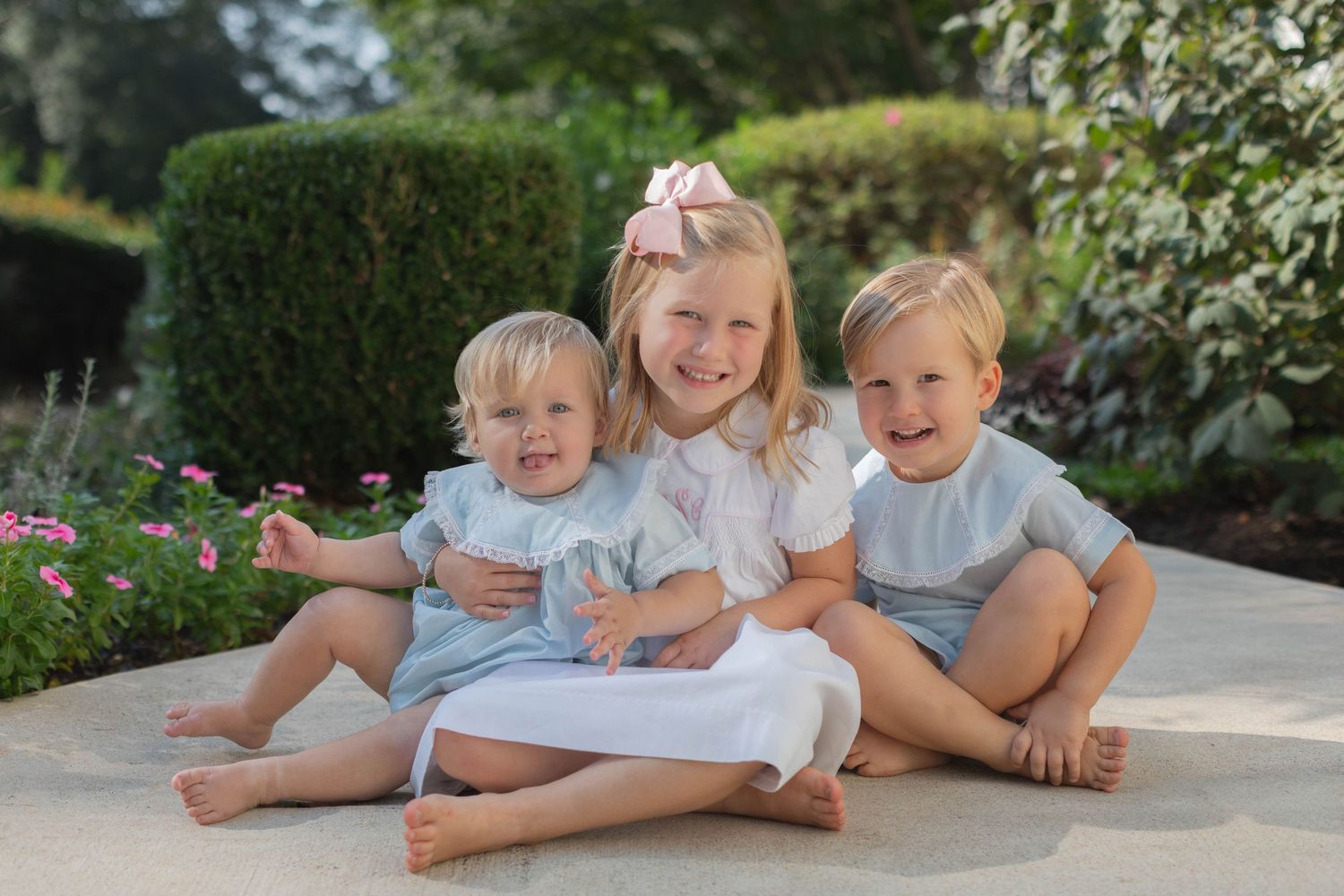 Group lounges casually outdoors in matching light blue and white outfits during a sunny garden photo session.