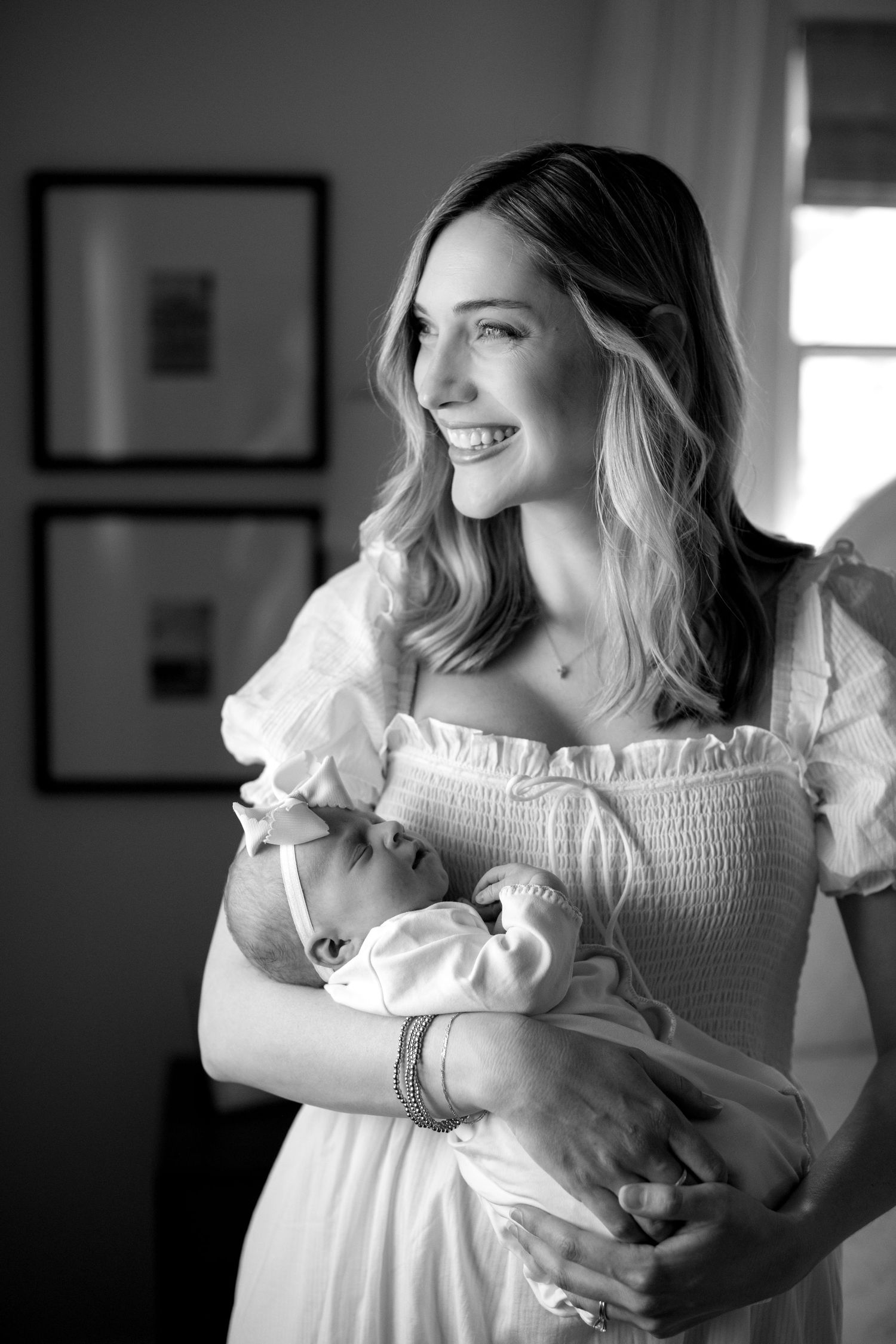 Mother in white dress holding newborn baby in black and white portrait.