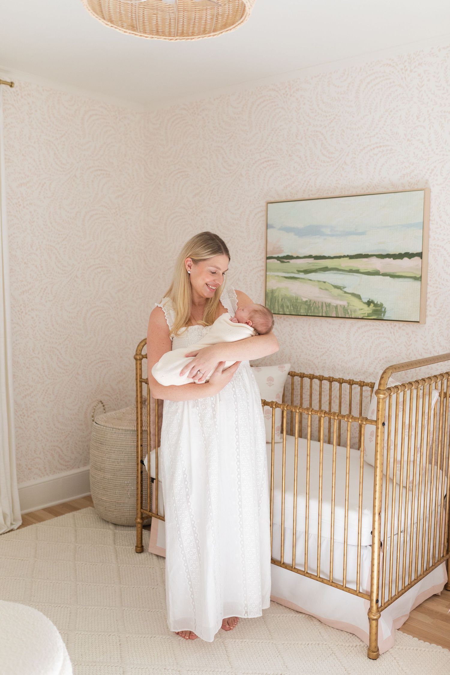Nursery room with gold crib and white bedding showcases soft natural lighting and coastal artwork on the wall.