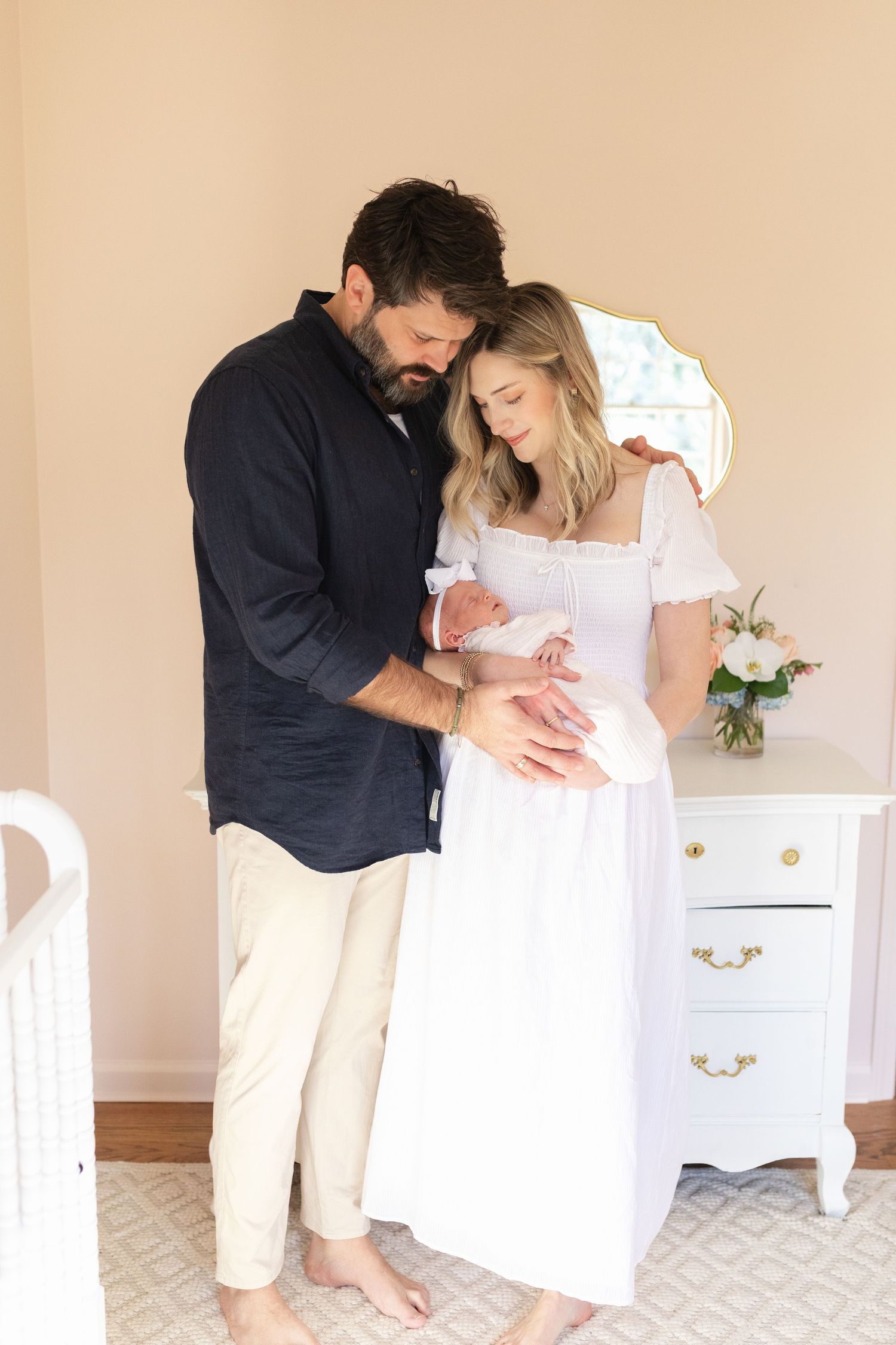 A couple shares an intimate moment with their newborn baby in front of a white dresser.