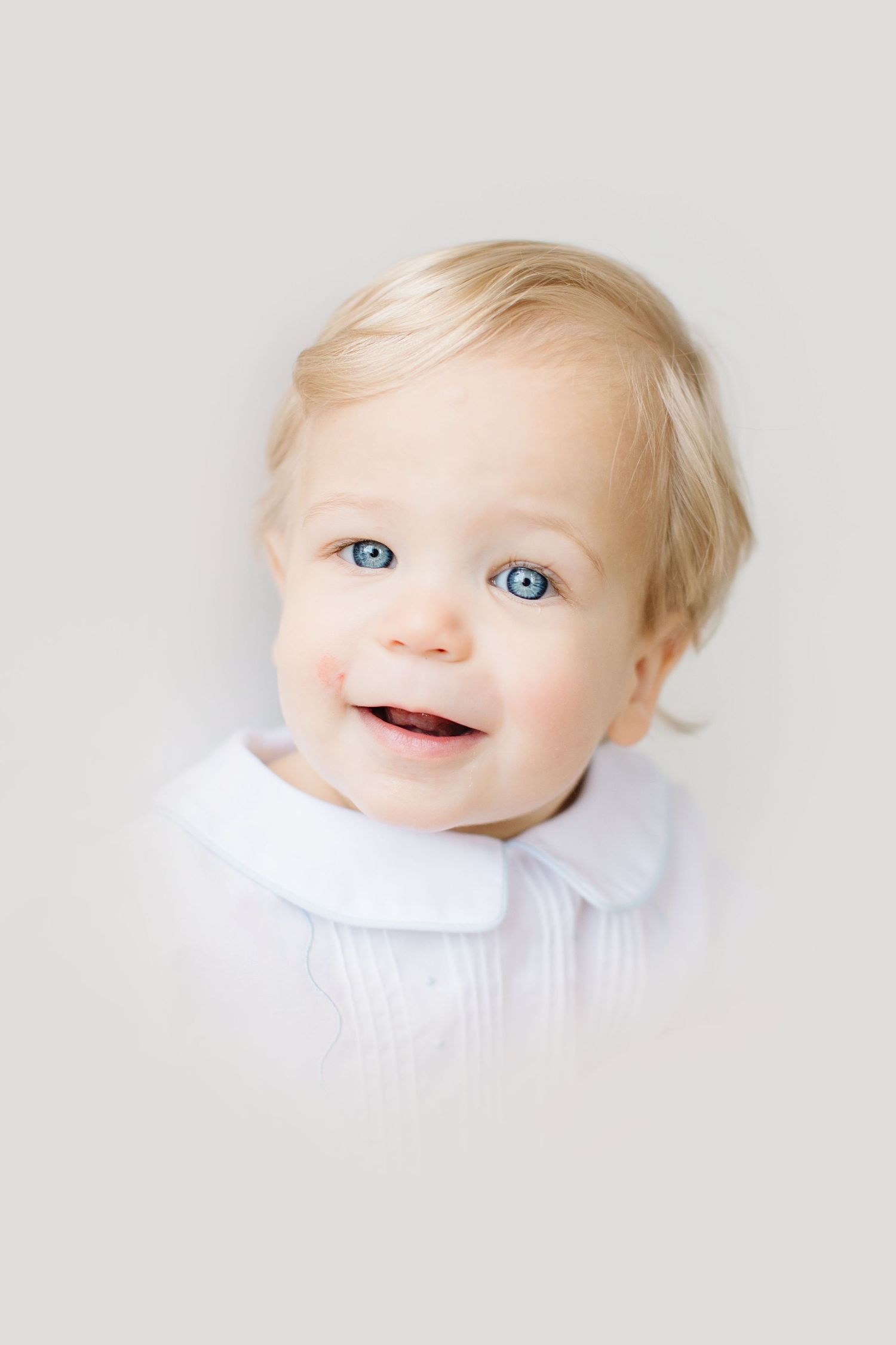 Three photos of a smiling baby with blonde hair and blue eyes wearing white against a light background.