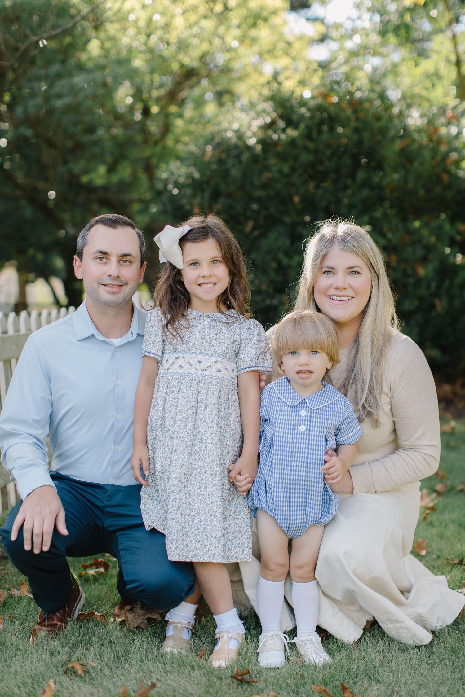 A family group sits together on grass in coordinated blue and white outfits during an outdoor photo session.