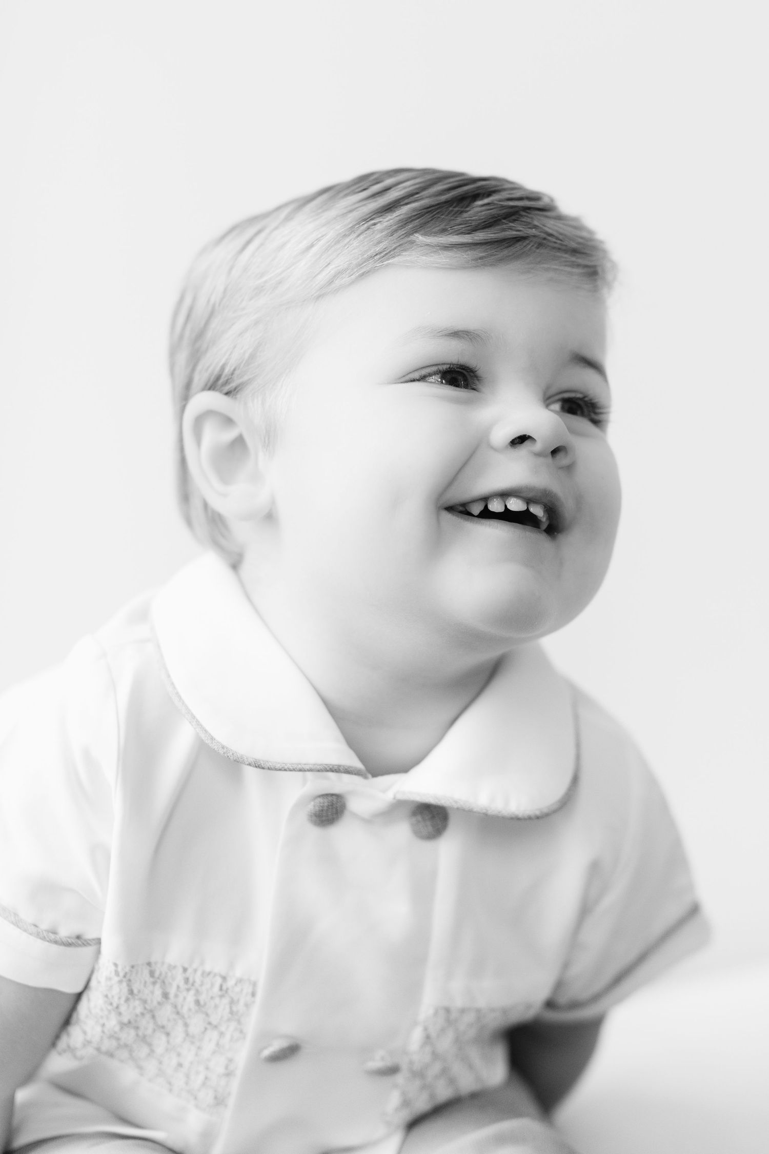 Black and white portrait series of a baby in white clothing looking up with joyful expressions.