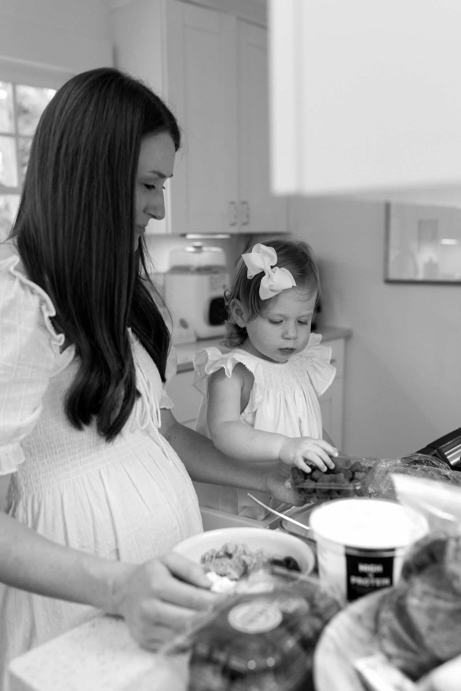 Parent and child in white dresses work together in kitchen preparing food at counter.