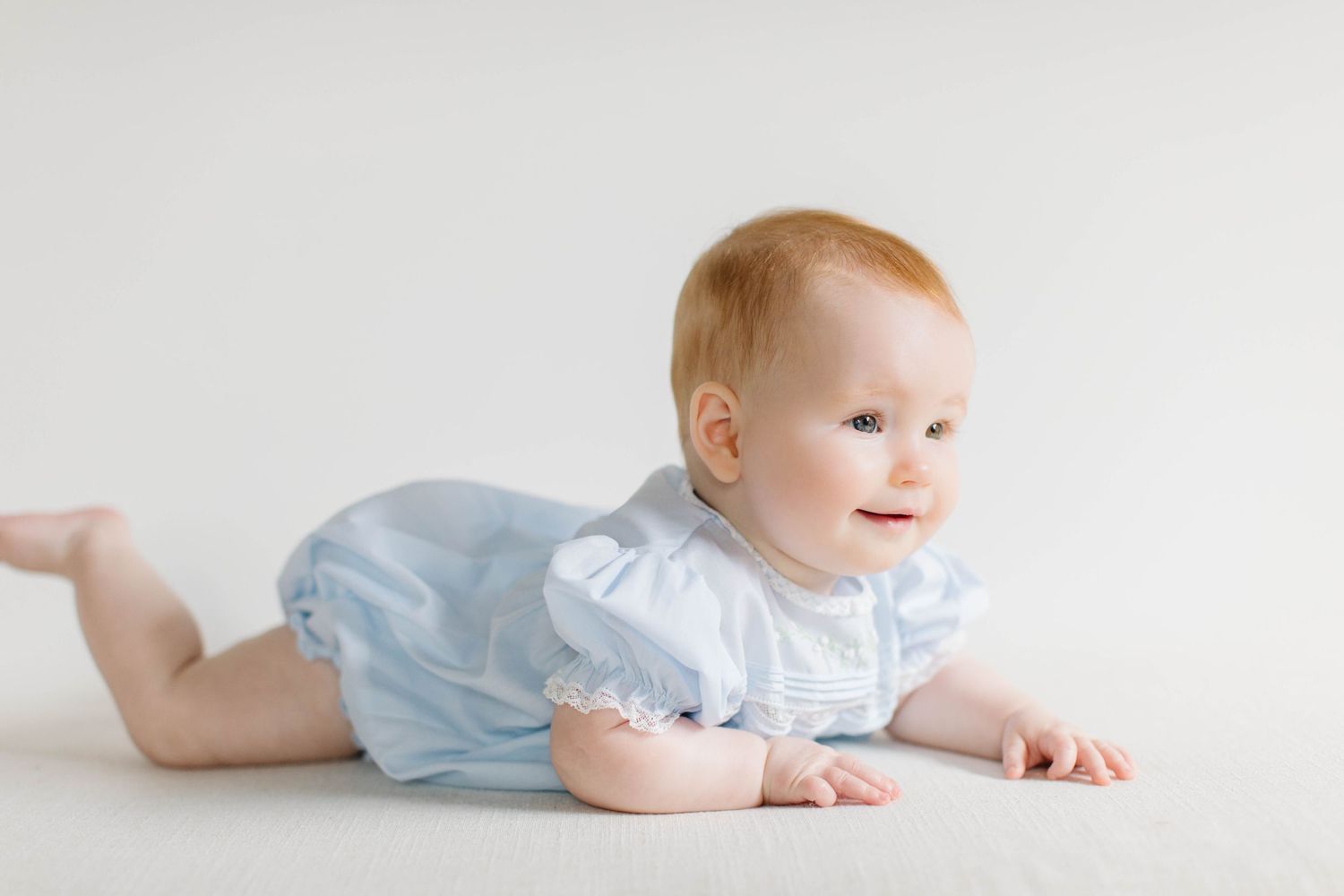 A young child in light blue dress clothing crawls playfully across a white backdrop in a series of photos.