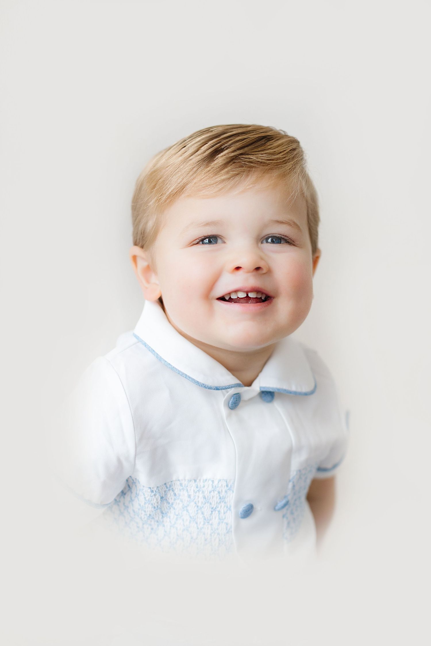 A baby in a white collared outfit smiles joyfully in a series of four connected portrait photos.