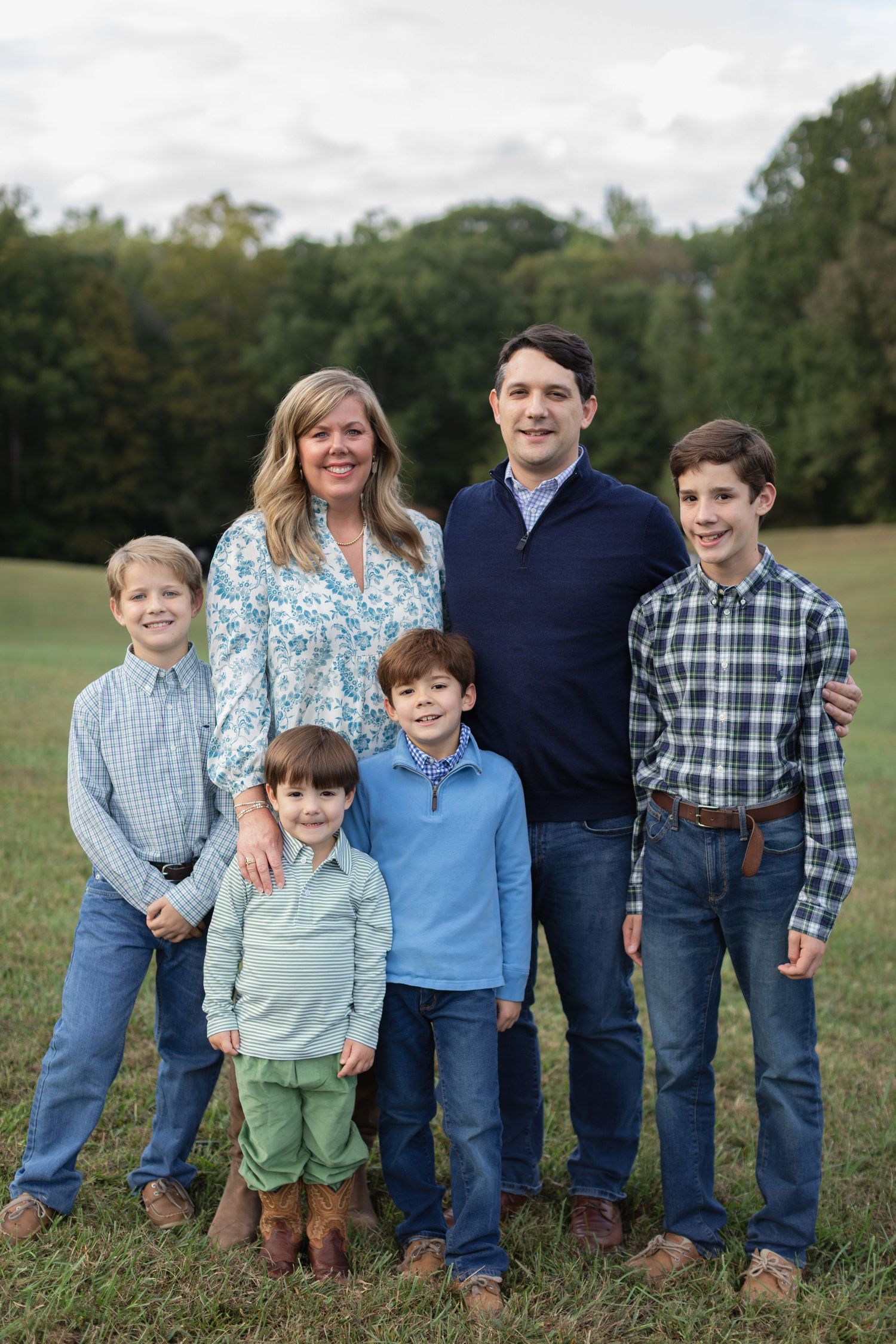A family group poses together outdoors in coordinating blue and plaid outfits in a grassy field.