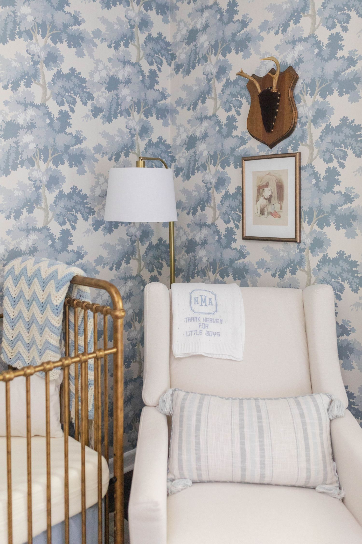 A cozy nursery nook with a cream glider chair and wooden crib against blue floral wallpaper - Atlanta Interior Design Photography