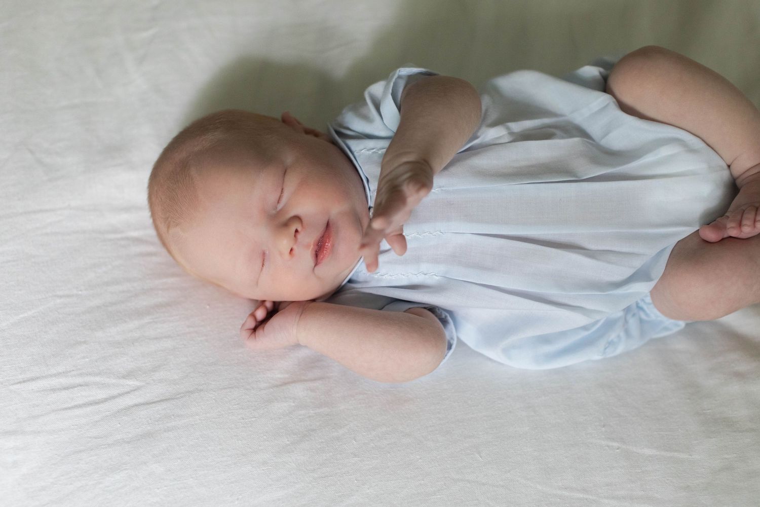 Newborn baby resting peacefully in soft white clothing against white bedding.
