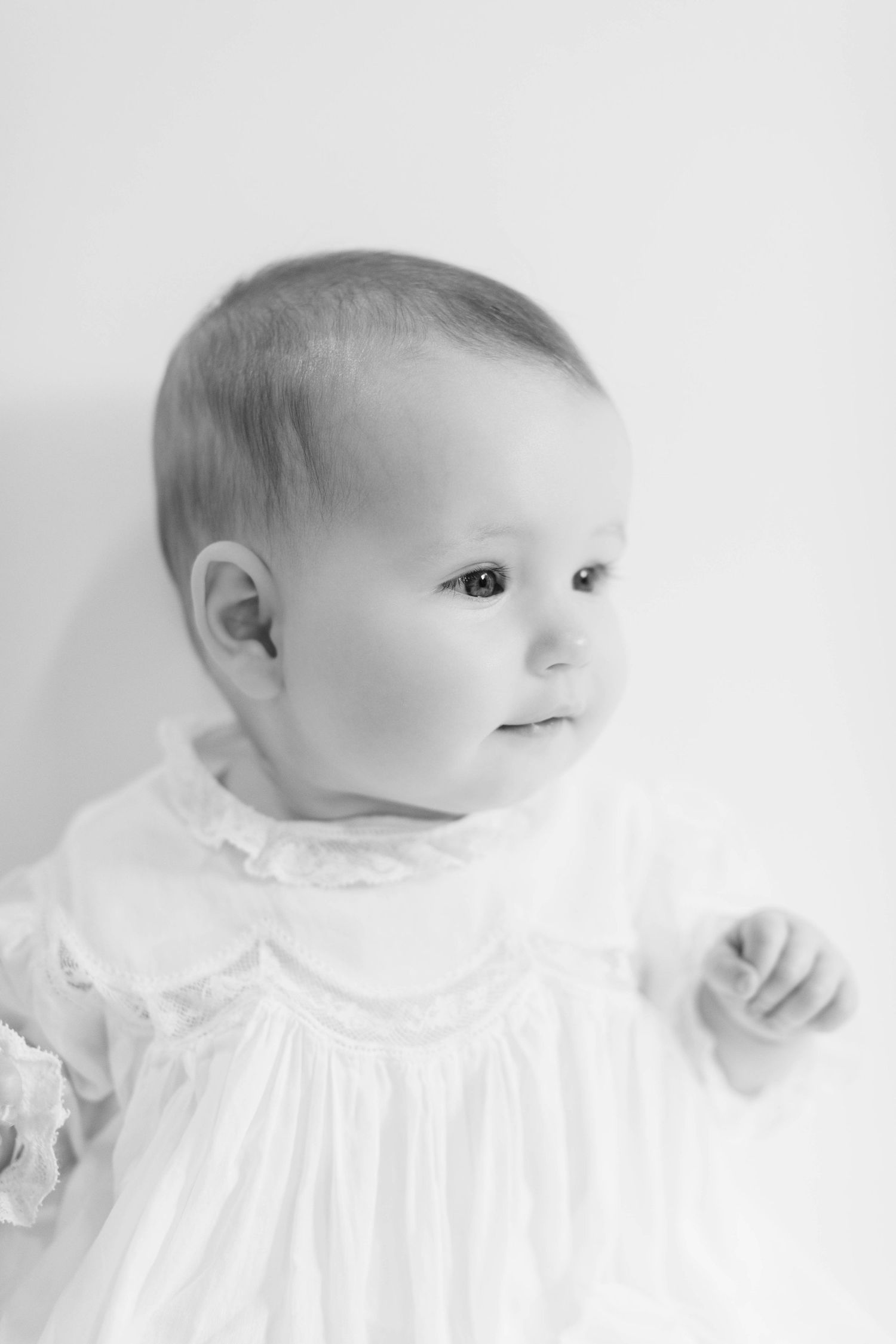 A series of soft black and white photographs showing different angles of an infant wearing a white christening gown.