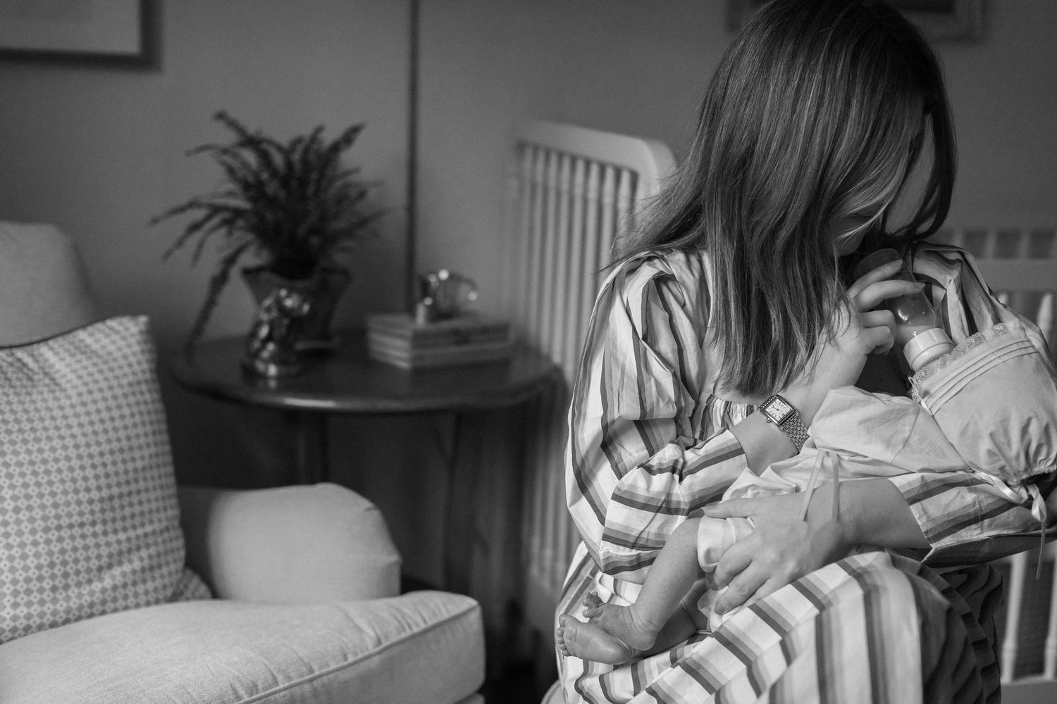 Black and white photo of parent in striped dress holding and bonding with newborn baby in nursery.