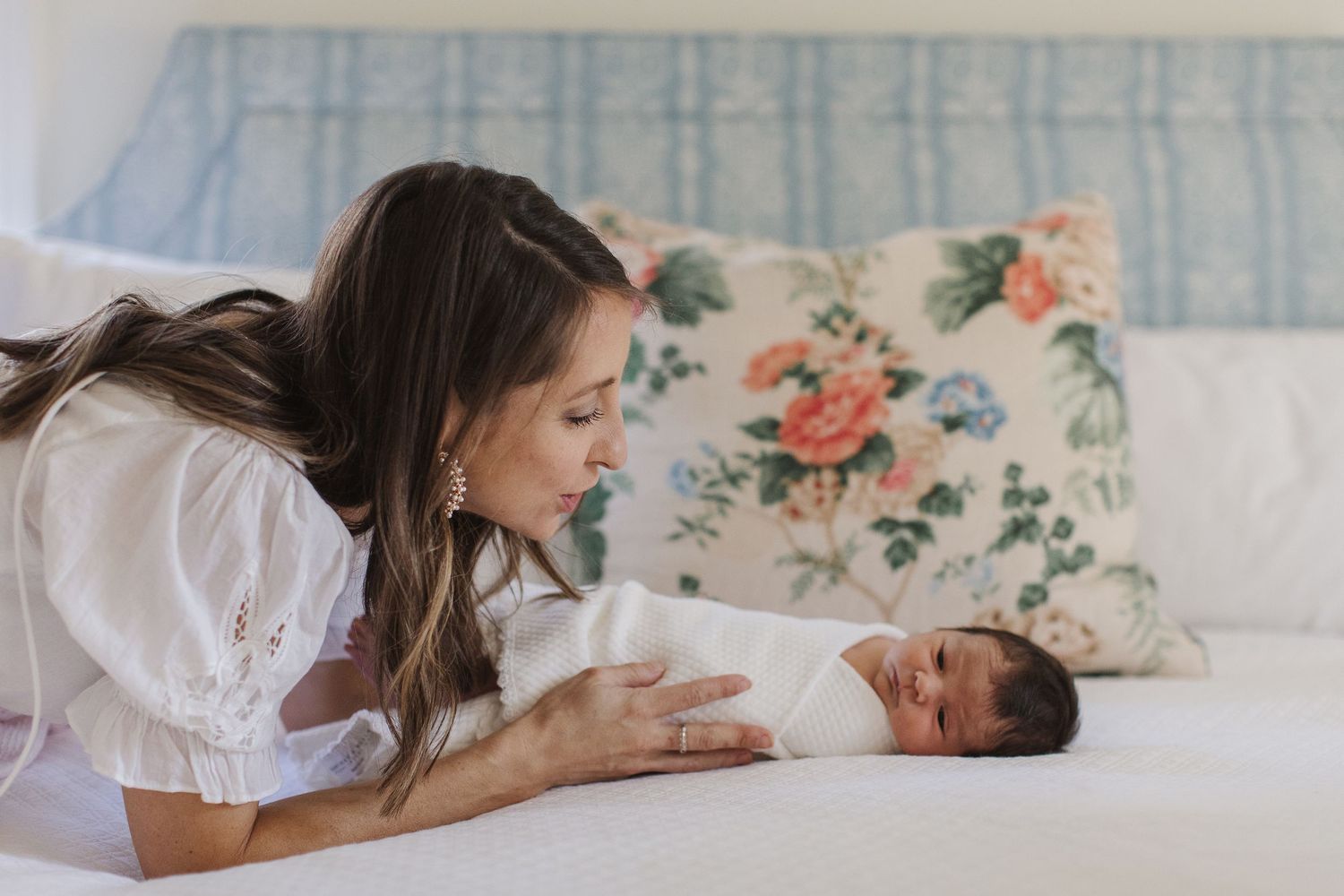 Gentle interaction with newborn baby on couch with floral pillow.