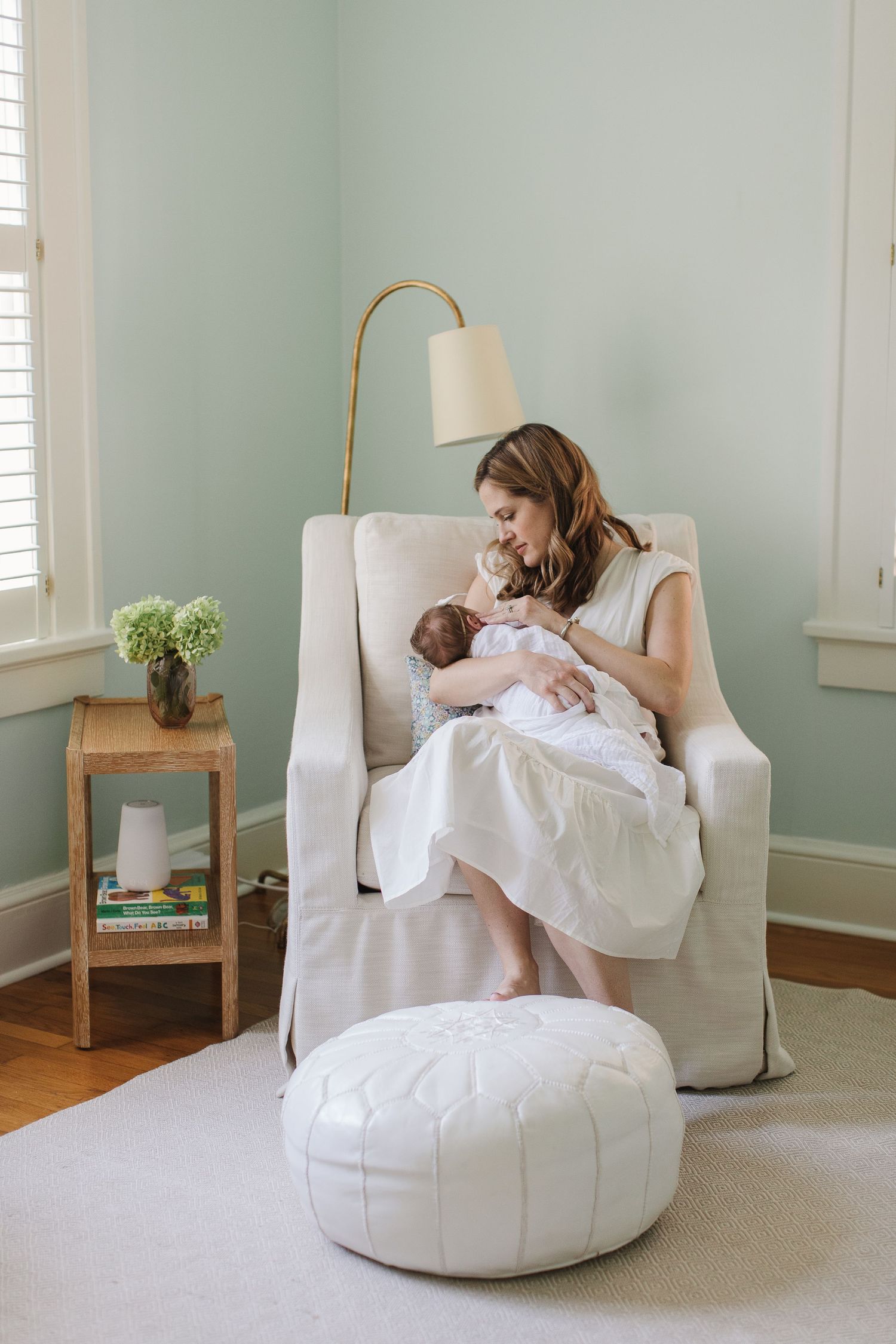Parent and baby sharing quiet moments in white slipcovered chair in minimalist nursery.