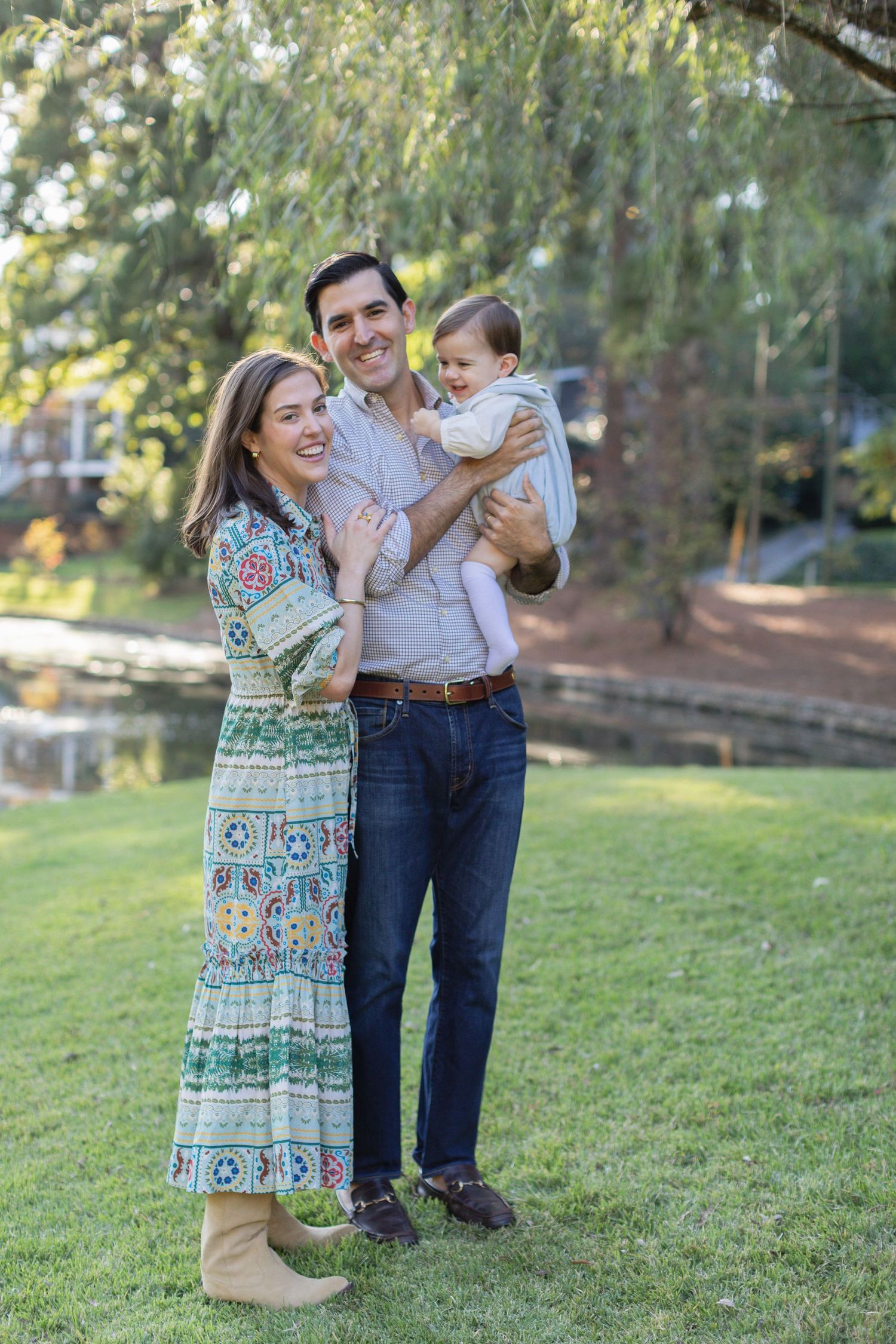 A family enjoys a tender moment together while standing on grass in a park during golden hour.