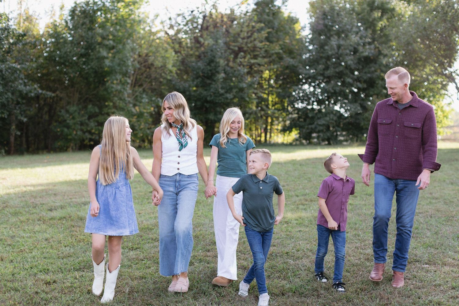 A group of people walking together on a grassy hill in casual attire during a sunny autumn day.