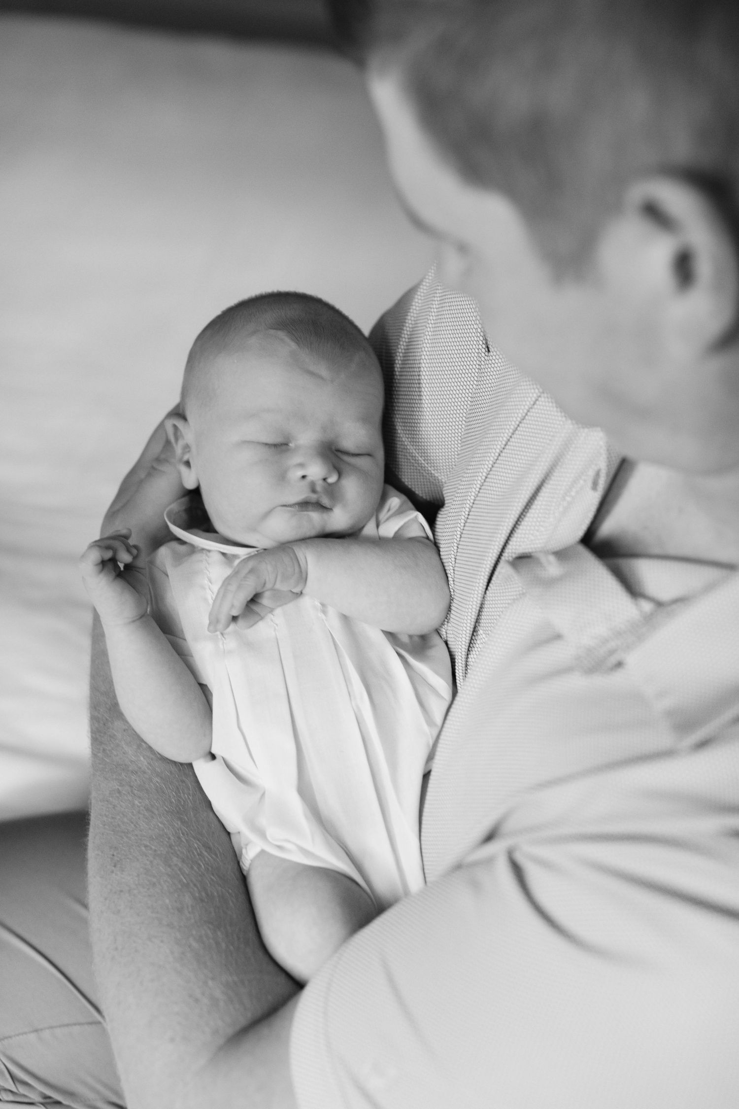 A peaceful sleeping newborn baby rests in soft light wearing white clothing.