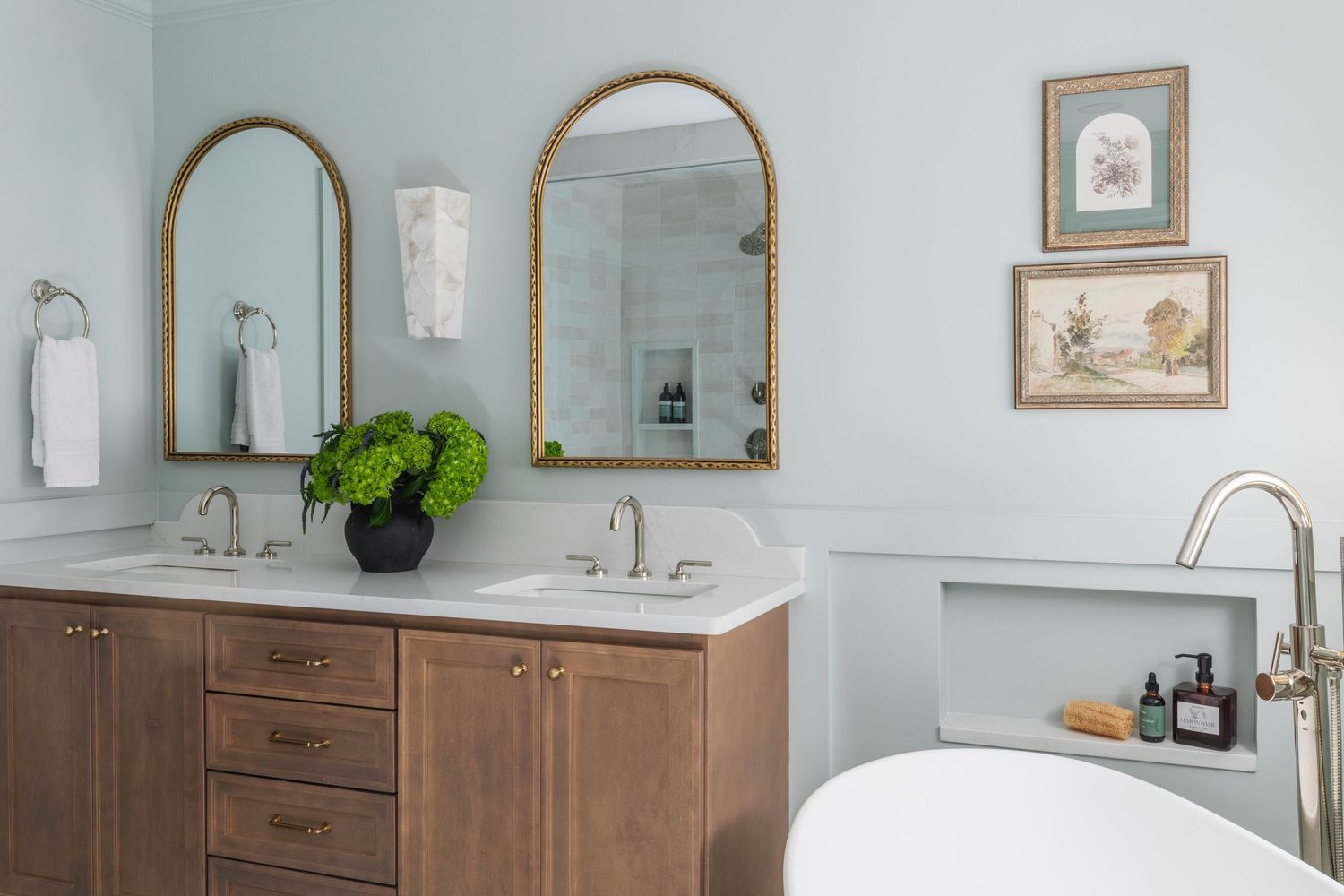 Spacious bathroom featuring dual arched mirrors, wood vanity and soaking tub.