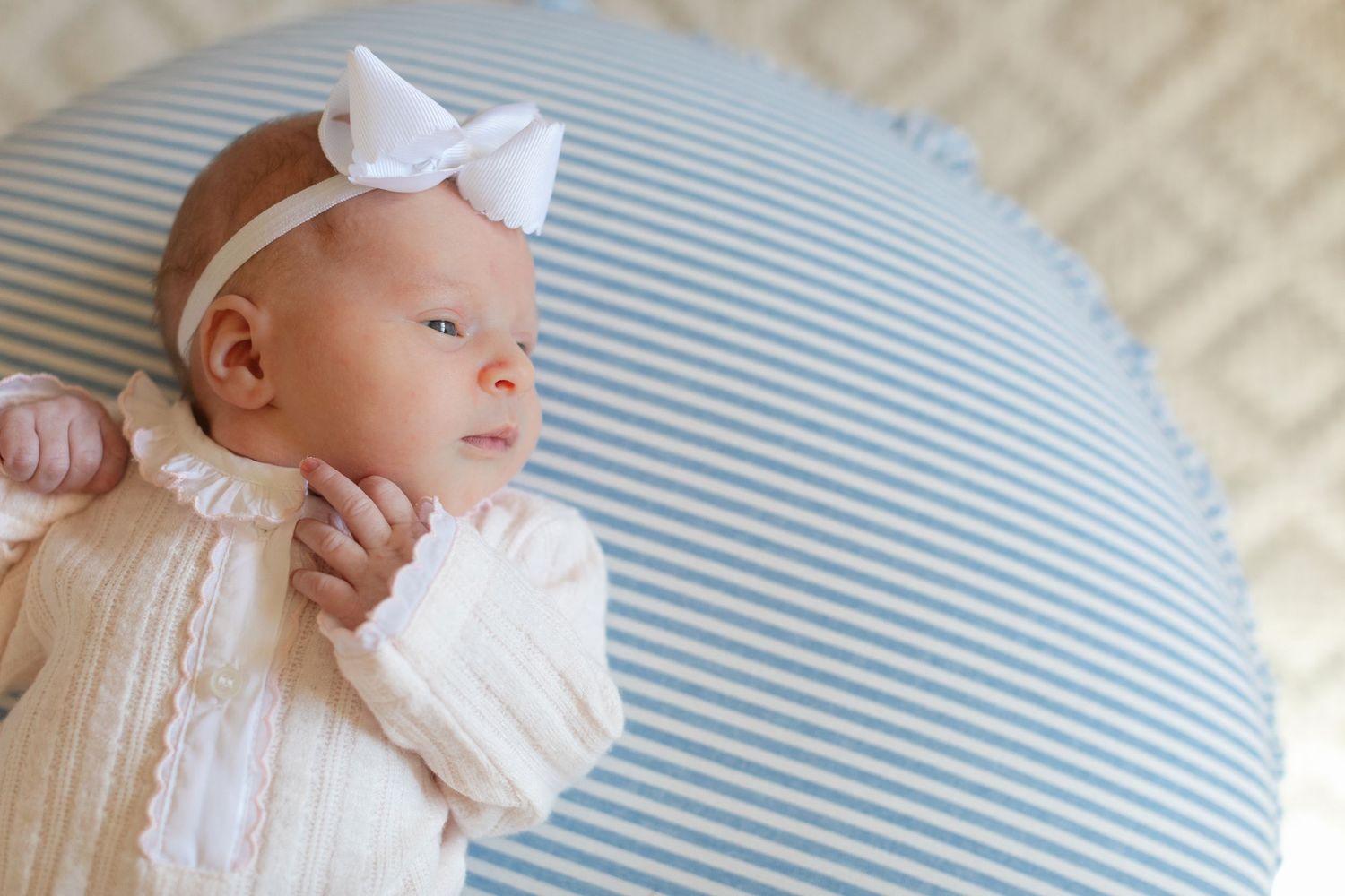 Newborn baby in white outfit resting on blue and white striped bedding during professional photo session.