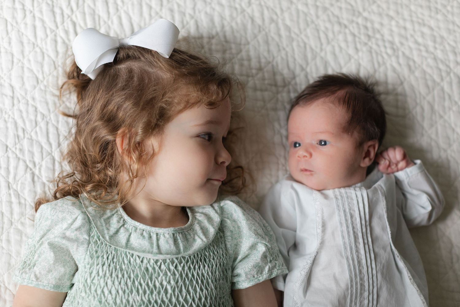 Two young children in mint green outfits lie together on a soft gray surface.