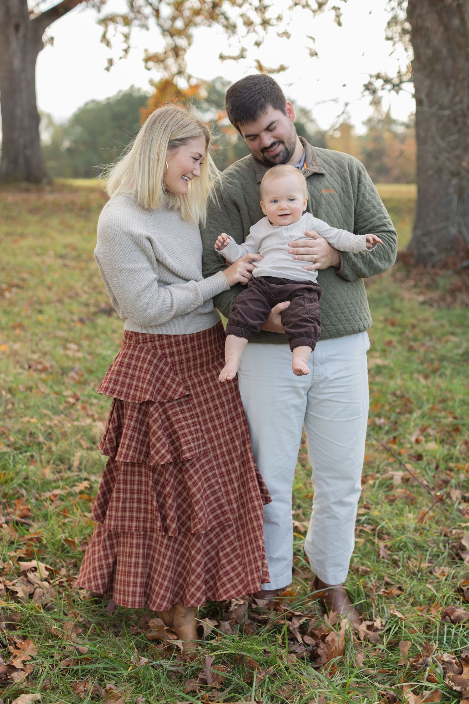 A family shares tender moments together on fallen autumn leaves in an outdoor setting.