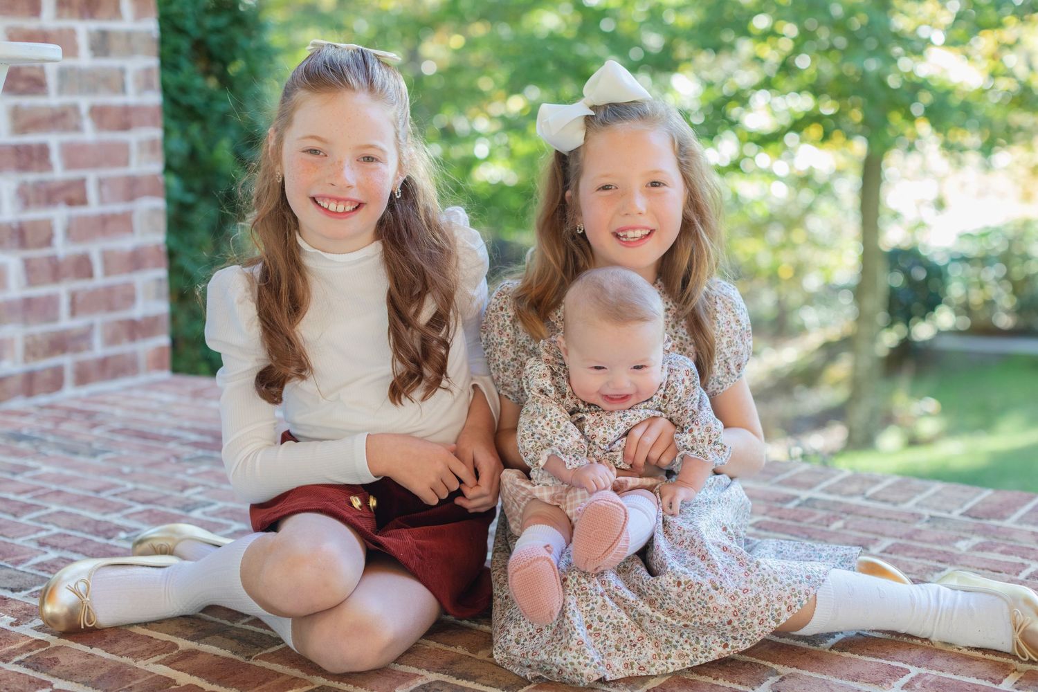 Three children sit together on brick steps while laughing and smiling during an outdoor family photo session.