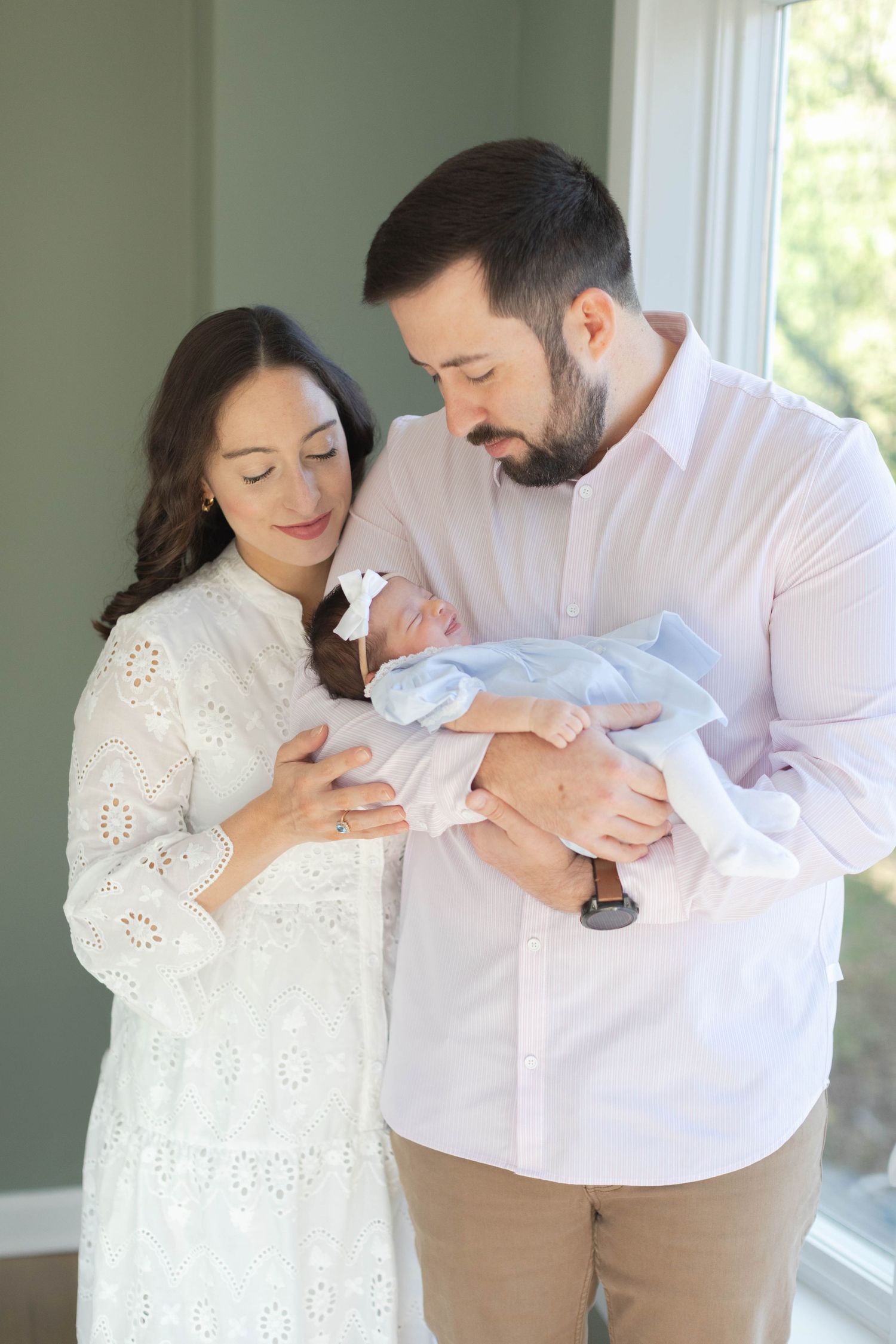 Tender moments between parents holding their newborn baby in a bright sunlit room.