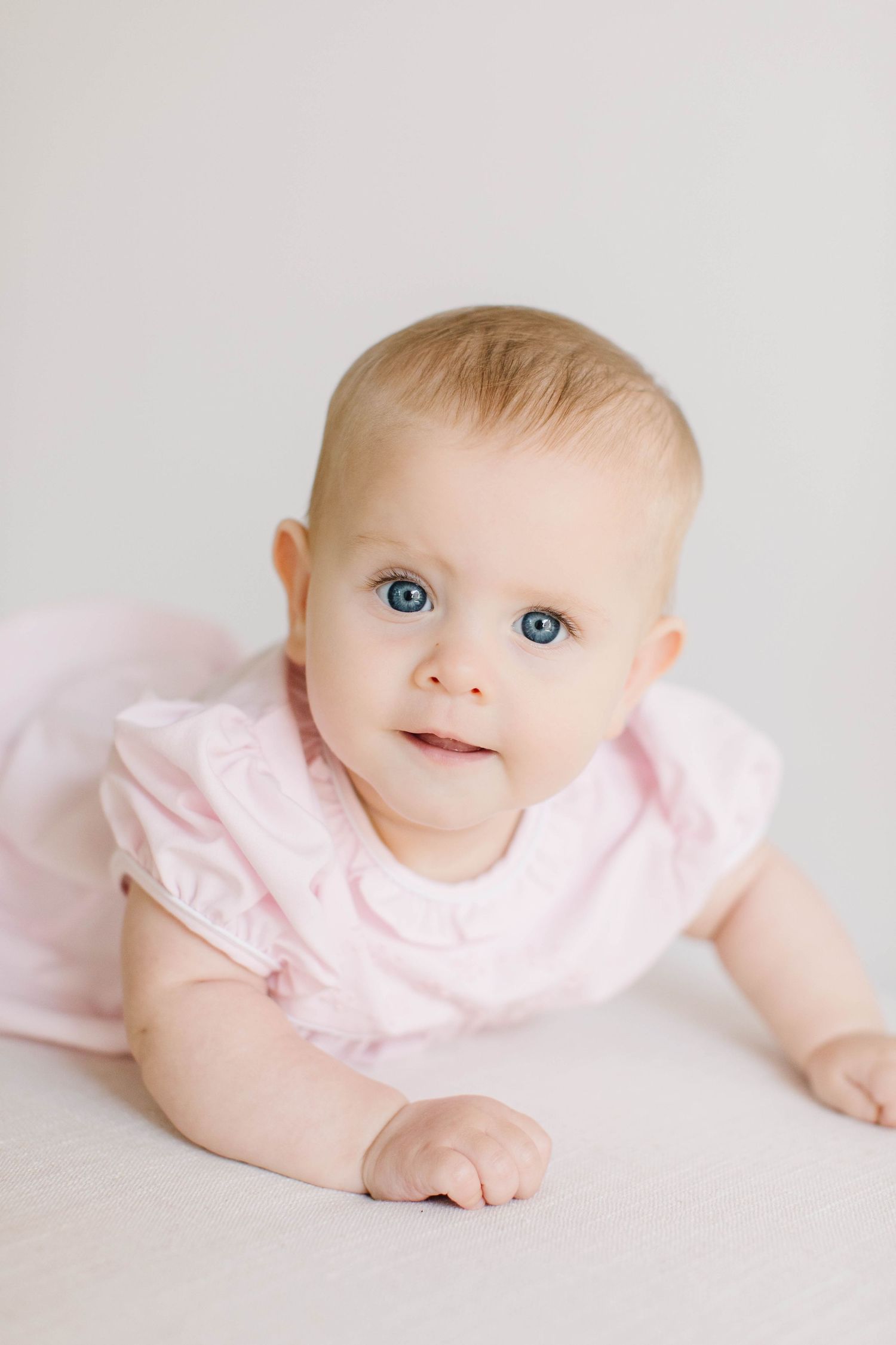 Sweet baby in pink ruffled dress laying on white background showcasing bright blue eyes.