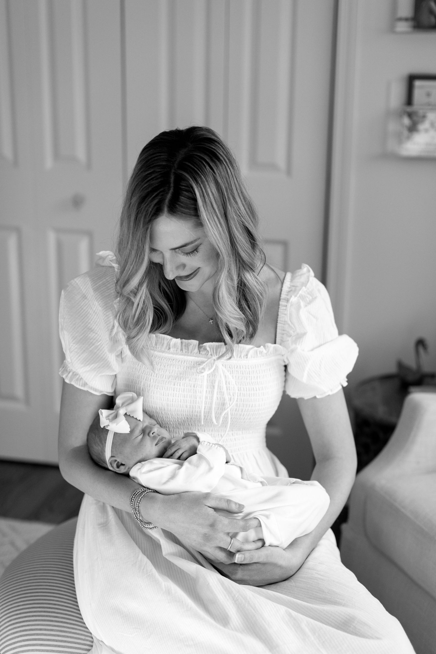 Woman in white dress holding newborn baby in peaceful indoor setting.
