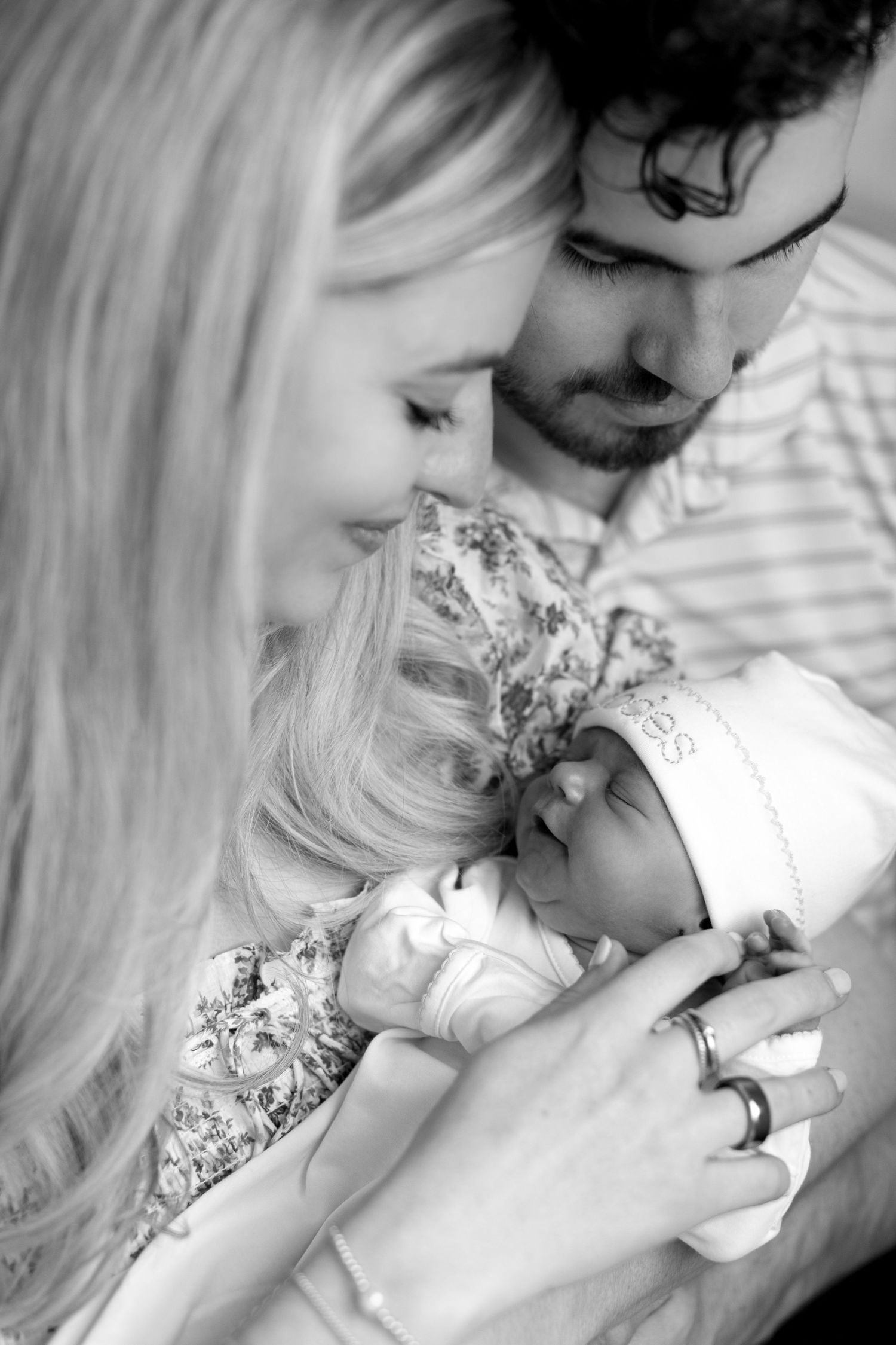 Black and white portrait of parents lovingly gazing at their sleeping newborn baby together.