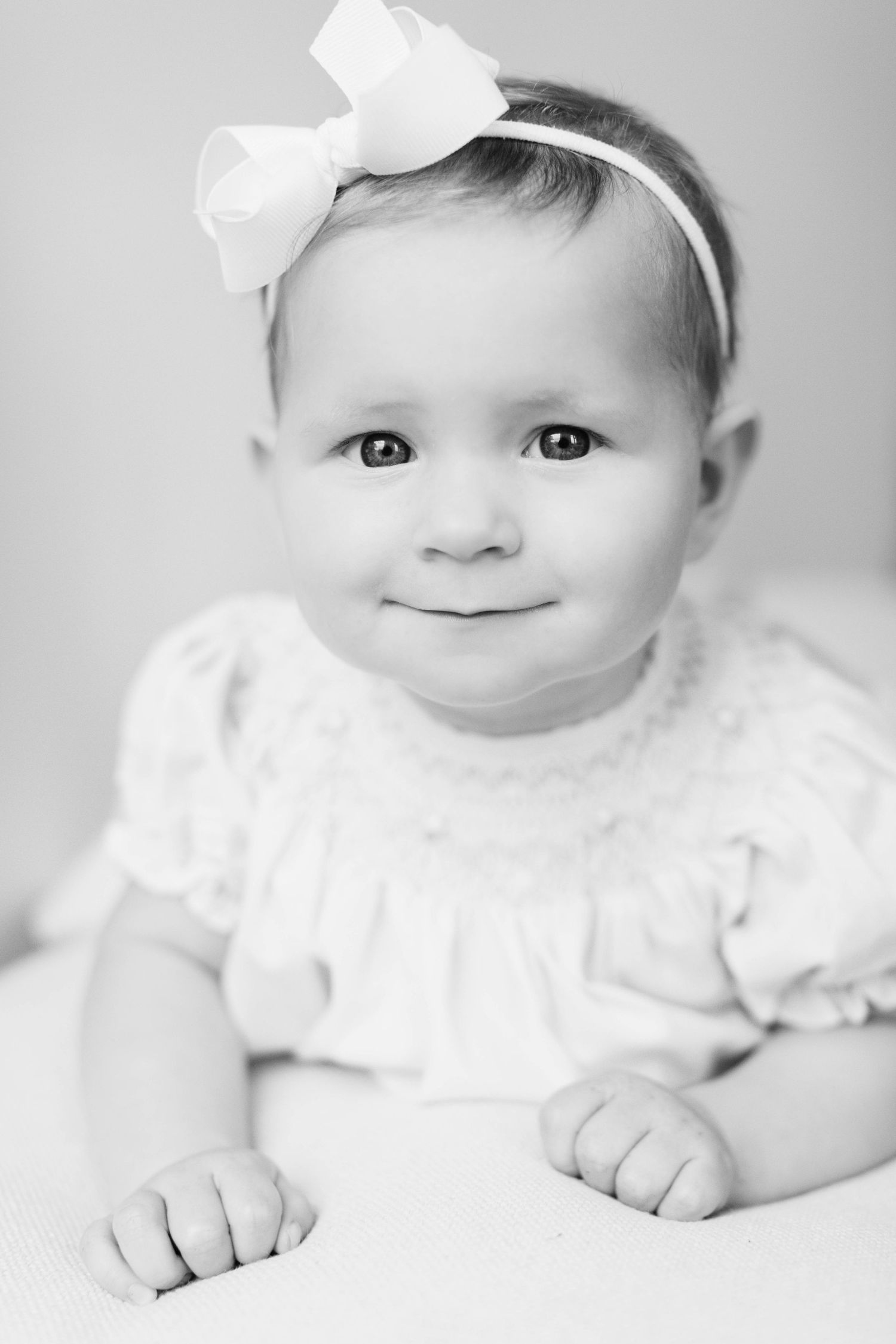 Sweet black and white portraits of a baby wearing white lace clothing and bow against soft white background.