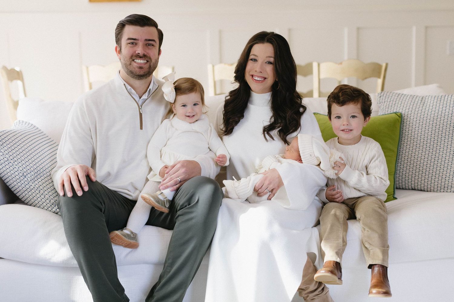 Family portrait showing warm interactions while seated on grey couch in bright living room.