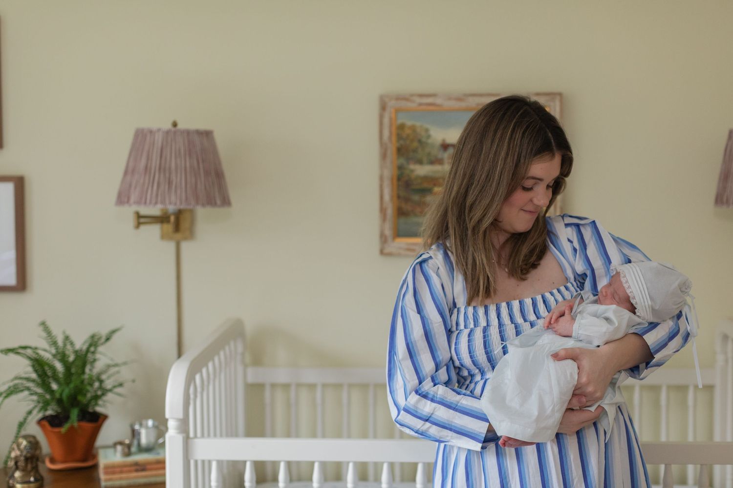 Person wearing striped dress cradles sleeping newborn baby against white crib background.