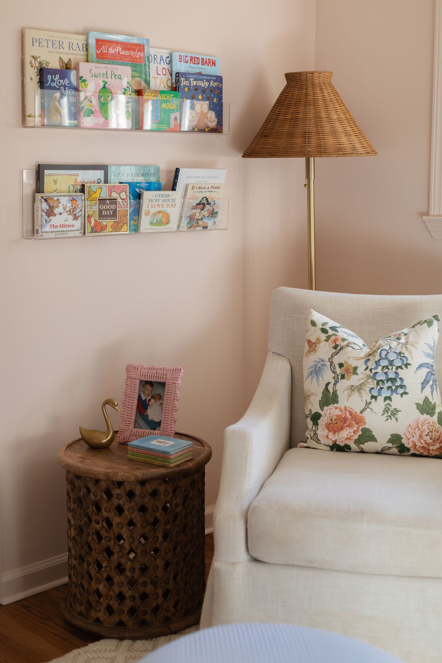 Cozy nursery corner featuring white seating, decorative pillows, and children's books displayed on wall shelves.
