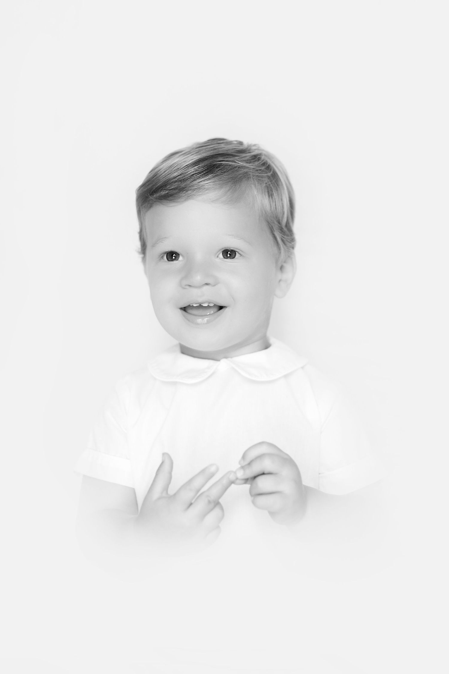 Adorable smiling toddler in white shirt posing for classic black and white portrait photo.