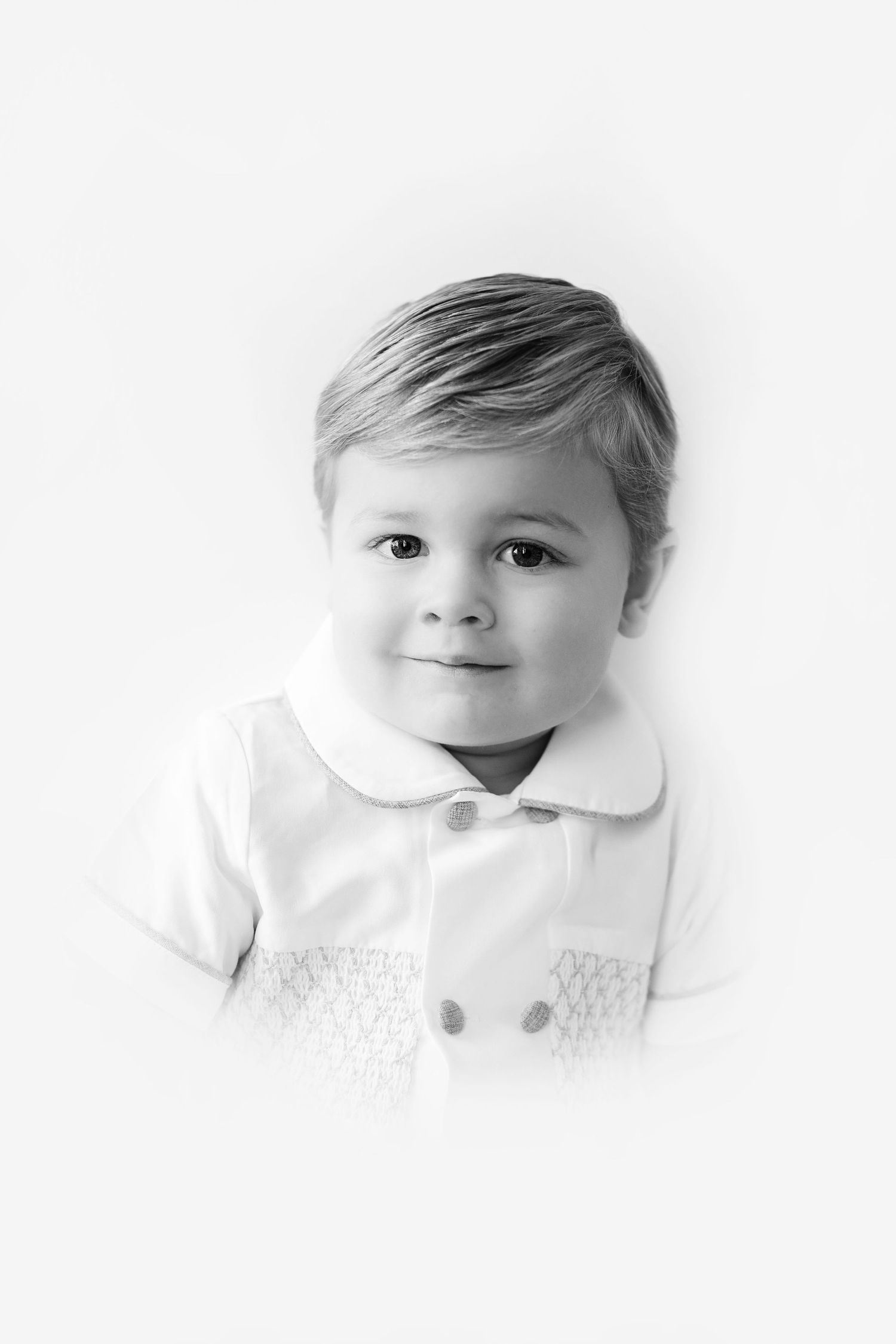 Black and white portrait of a young child wearing a white collared shirt with a gentle smile.