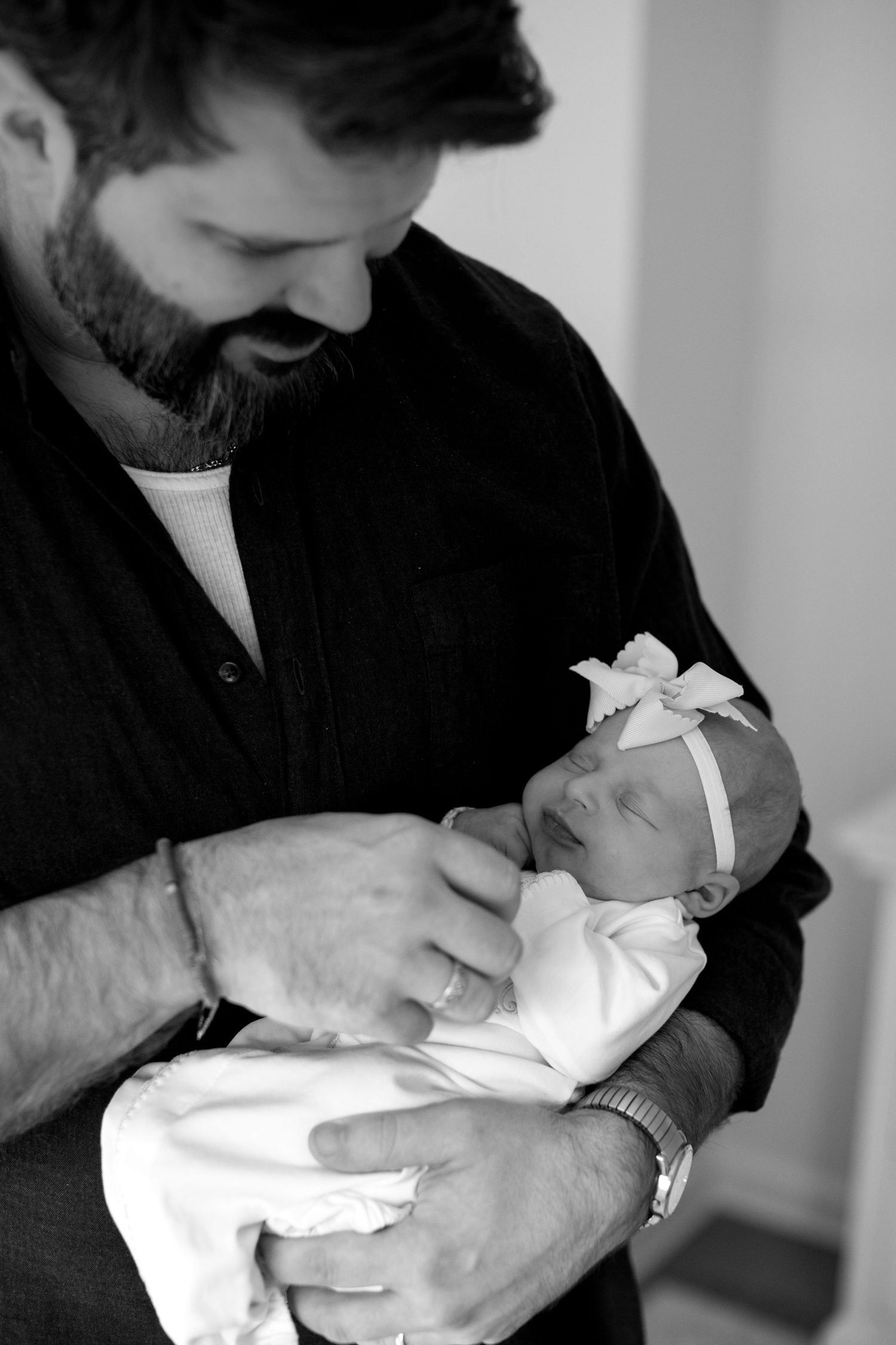 A black and white image of a parent tenderly cradling a sleeping newborn in white clothing.