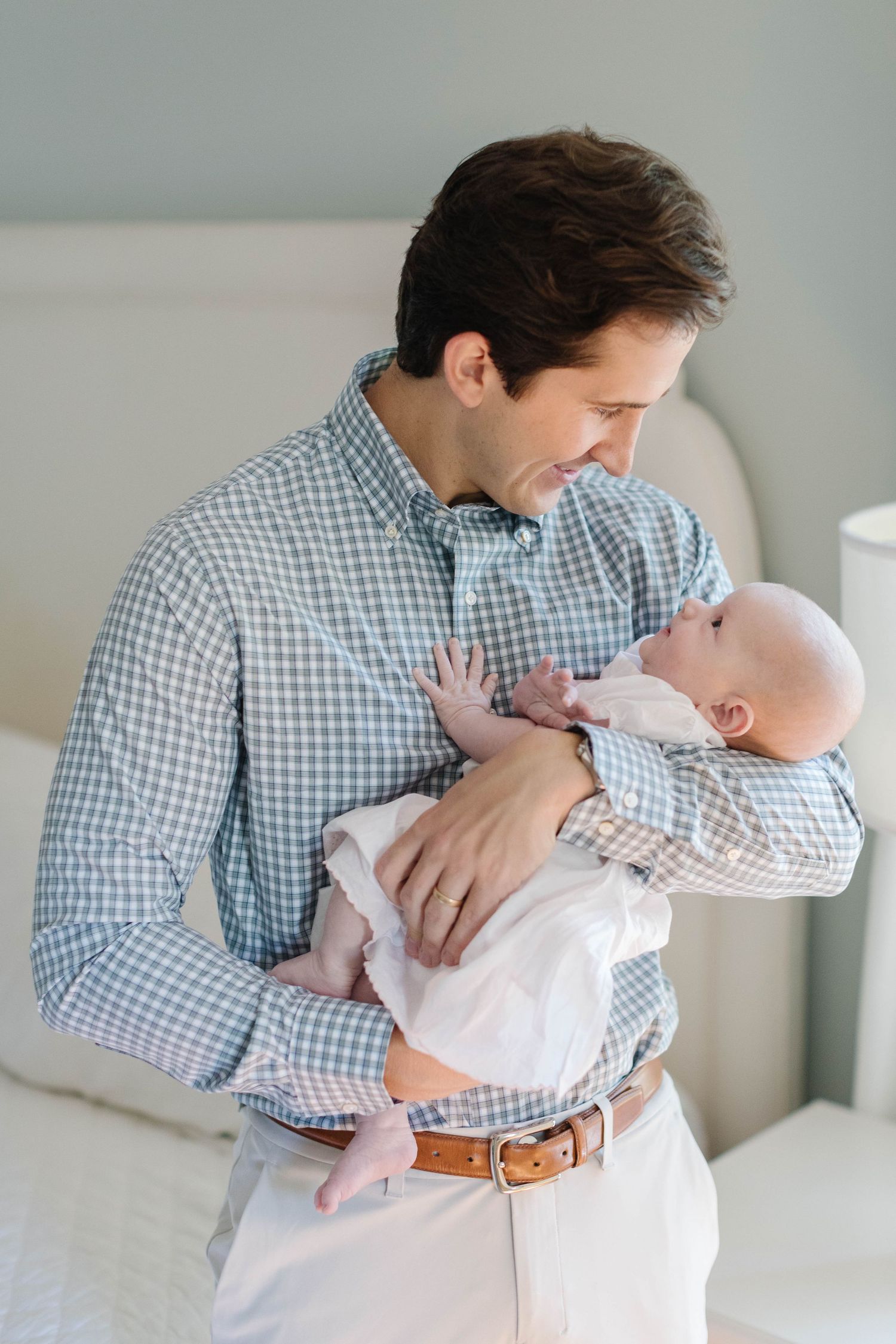 Intimate portrait of parent cradling newborn against light bedroom setting.