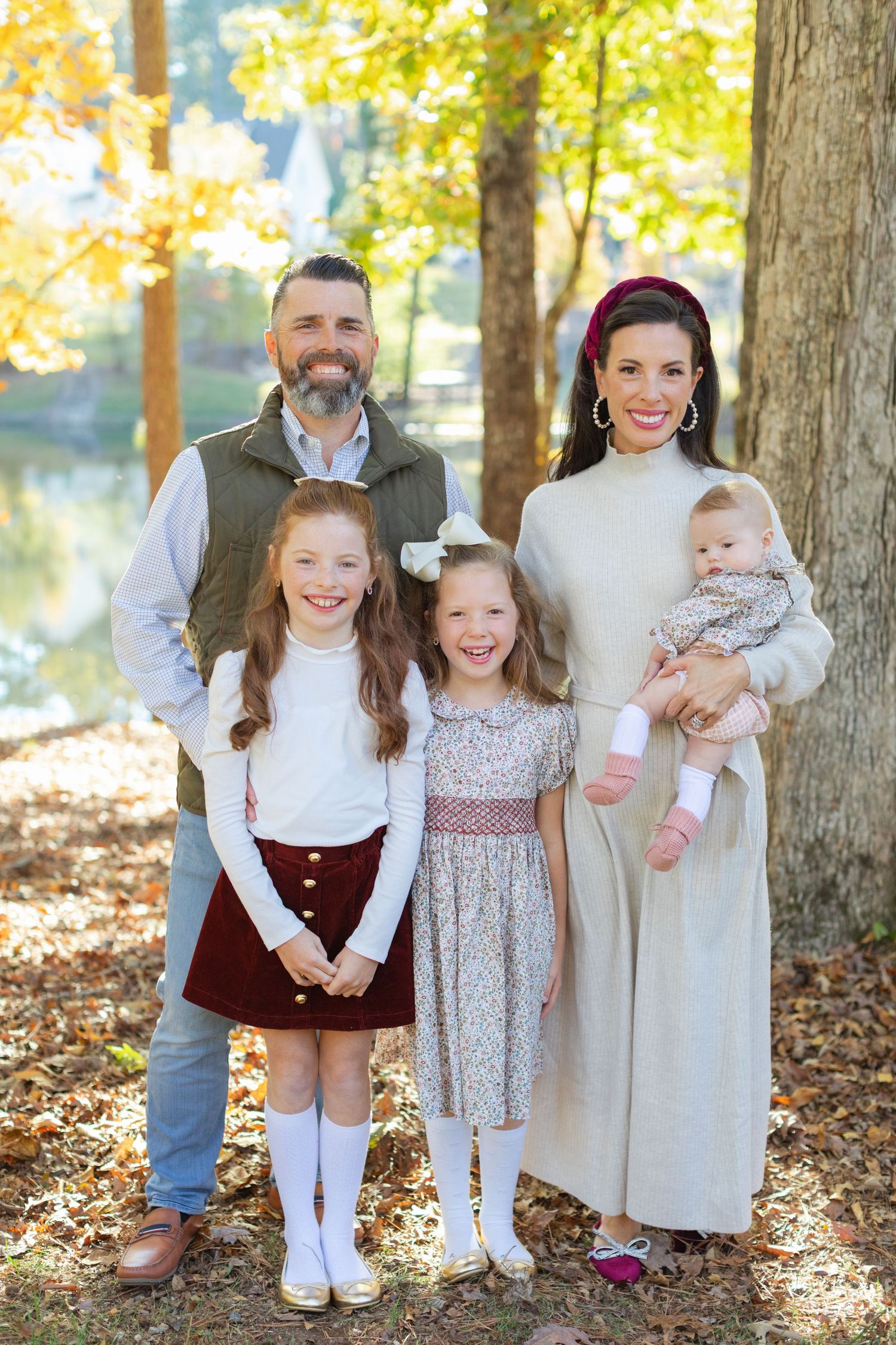A group poses together in a wooded outdoor setting during autumn with fallen leaves on the ground.