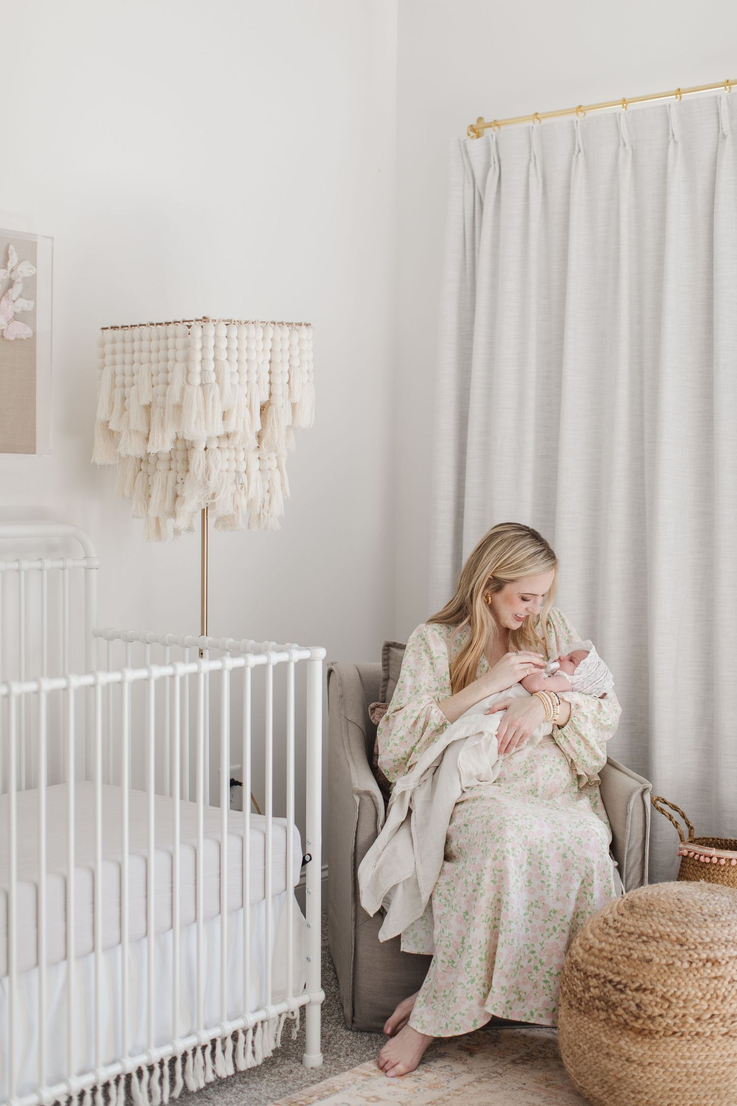 Nursery decorated in soft whites features woven chandelier, white crib, and cozy rocking chair.