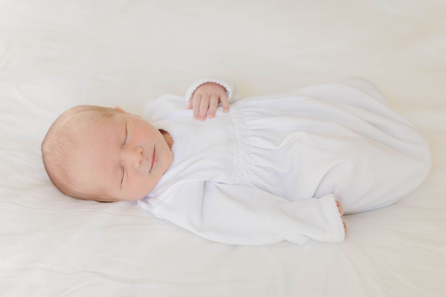 Peaceful newborn baby sleeping in white wrap against neutral background.